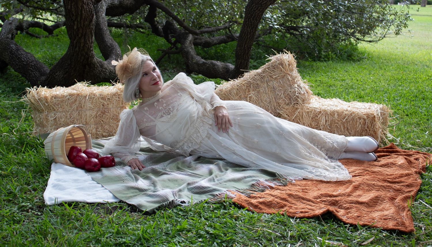 Woman in vintage white lace dress reclining on hay bales in a garden.