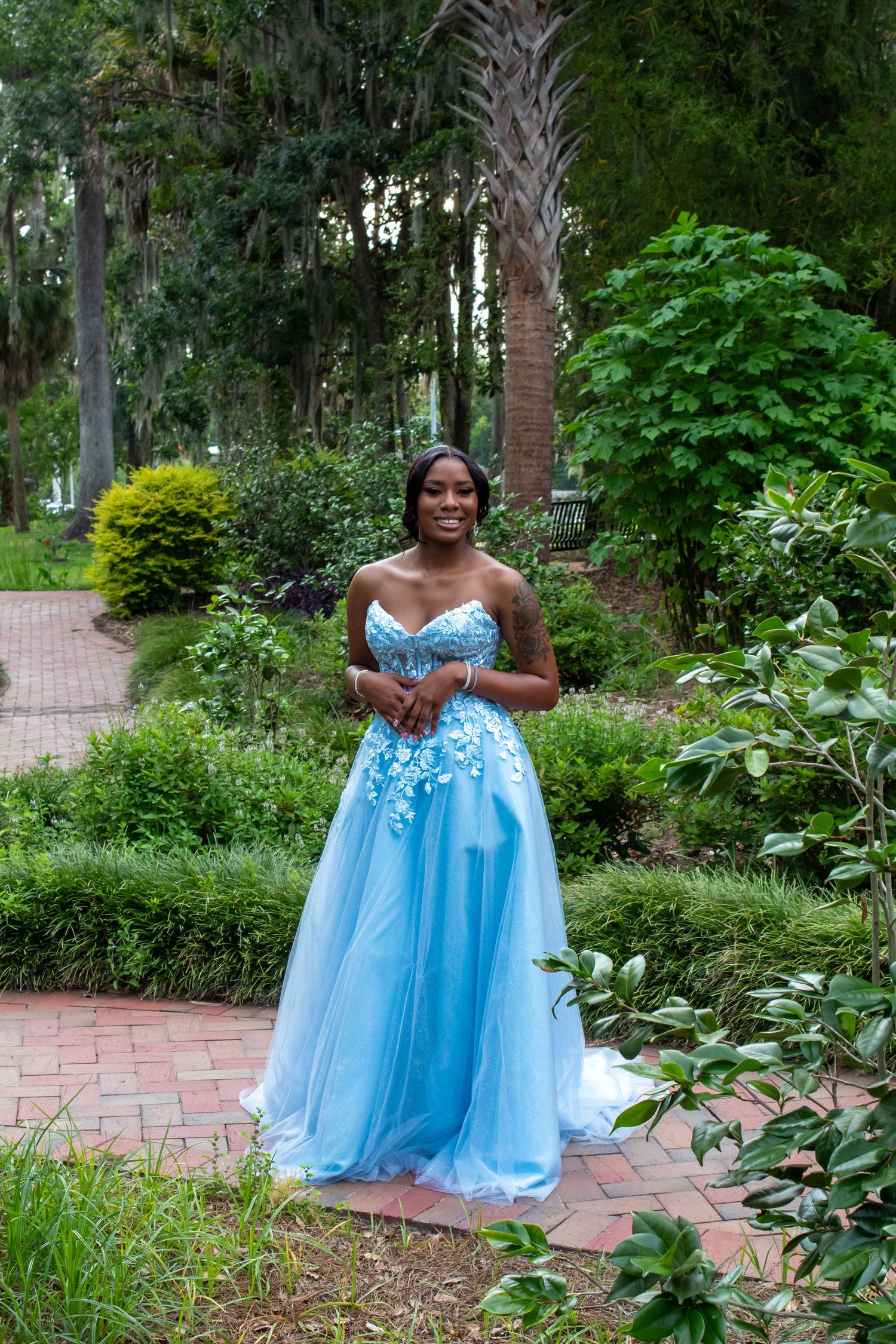 Young woman in blue floral ballgown posing in a lush garden setting.