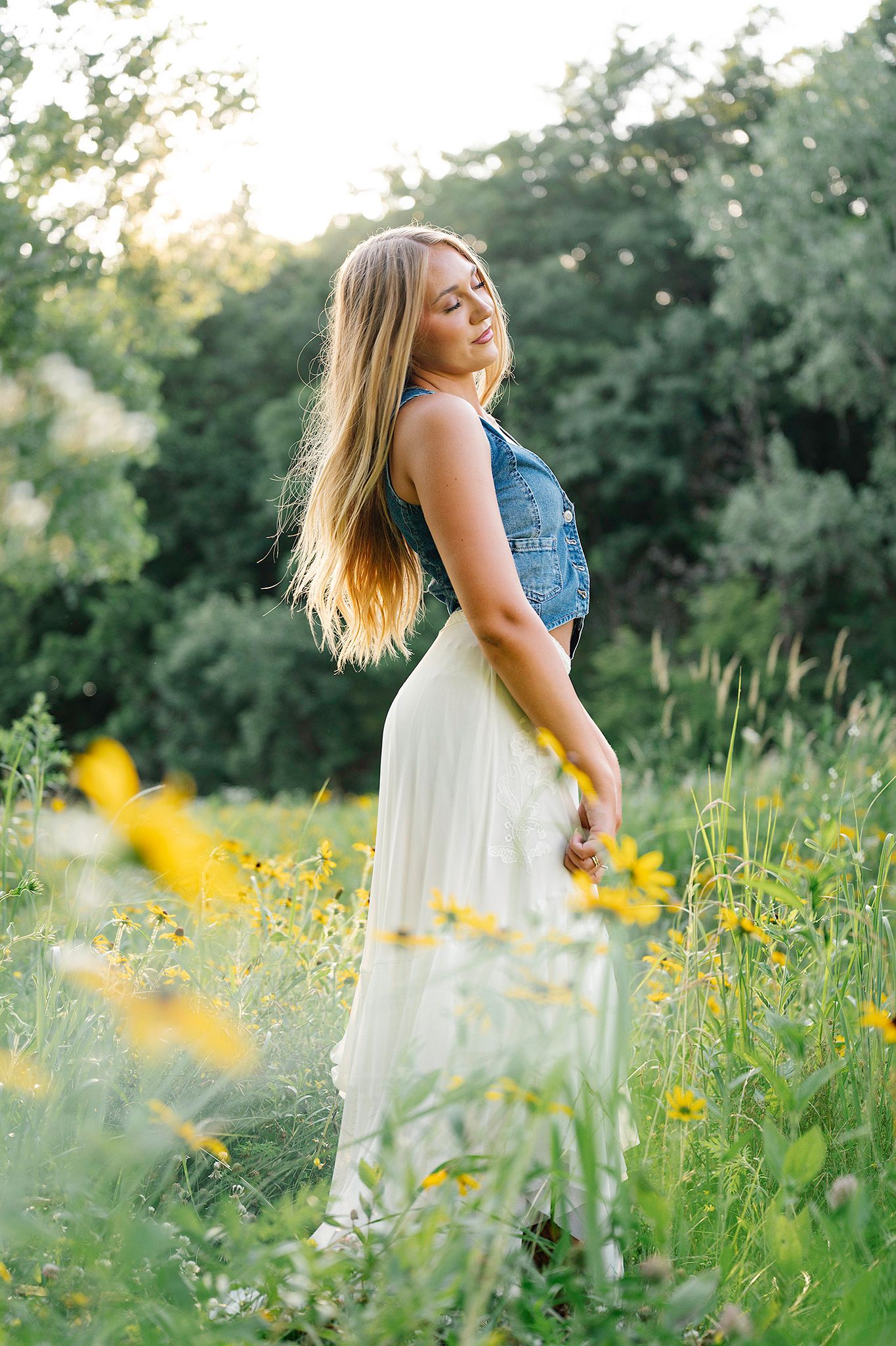 Blonde woman in denim vest and white skirt standing in a sunny wildflowers for Images by Merron, Ankeny & Des Moines senior photographer