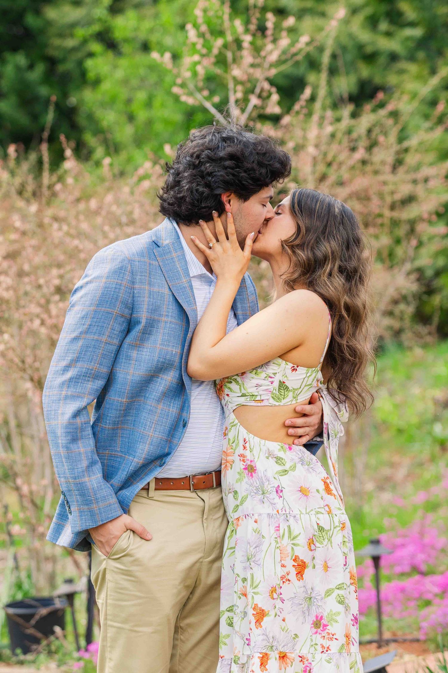 Couple sharing a romantic kiss outdoors, man in blue plaid blazer and woman in floral dress.