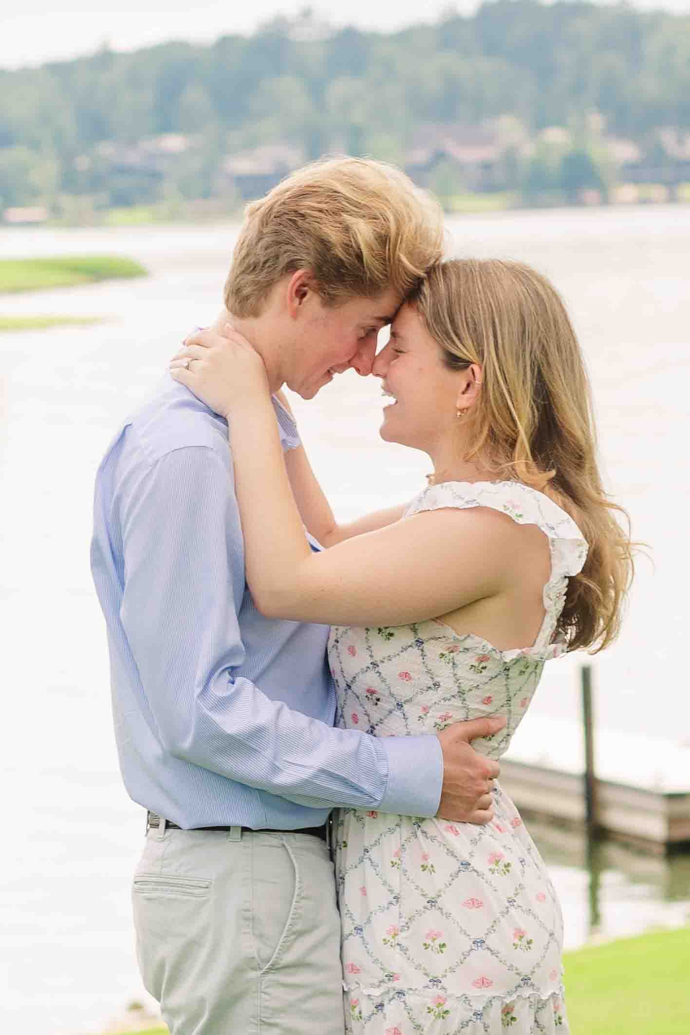 Happy couple touching foreheads and embracing by a lakeside dock, smiling joyfully at each other.