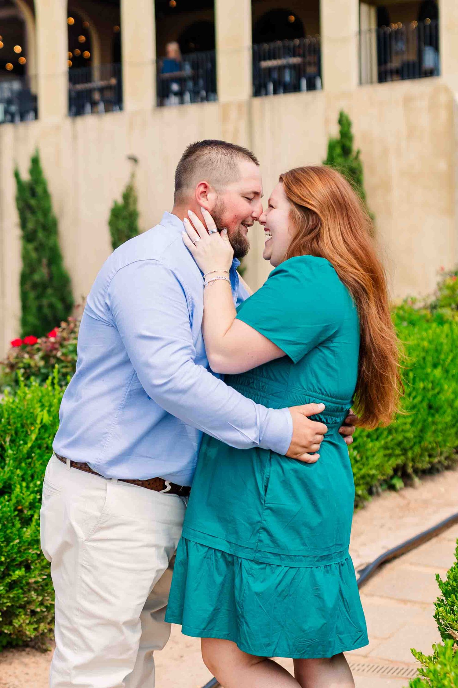 Joyful couple sharing a laugh and almost kissing in romantic garden setting outside winery with cypress trees.
