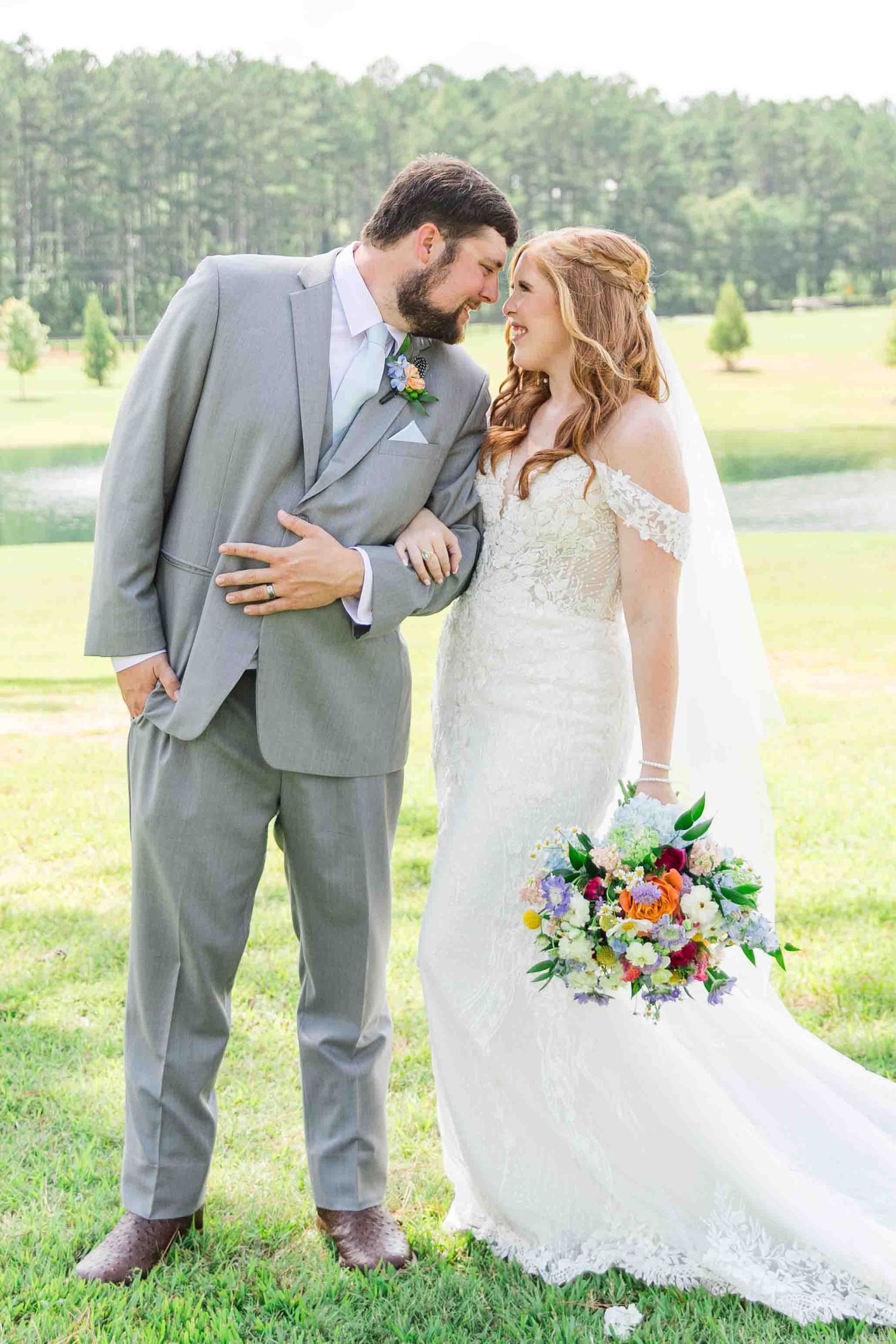 Bride and groom share romantic moment on golf course in gray suit and lace gown.