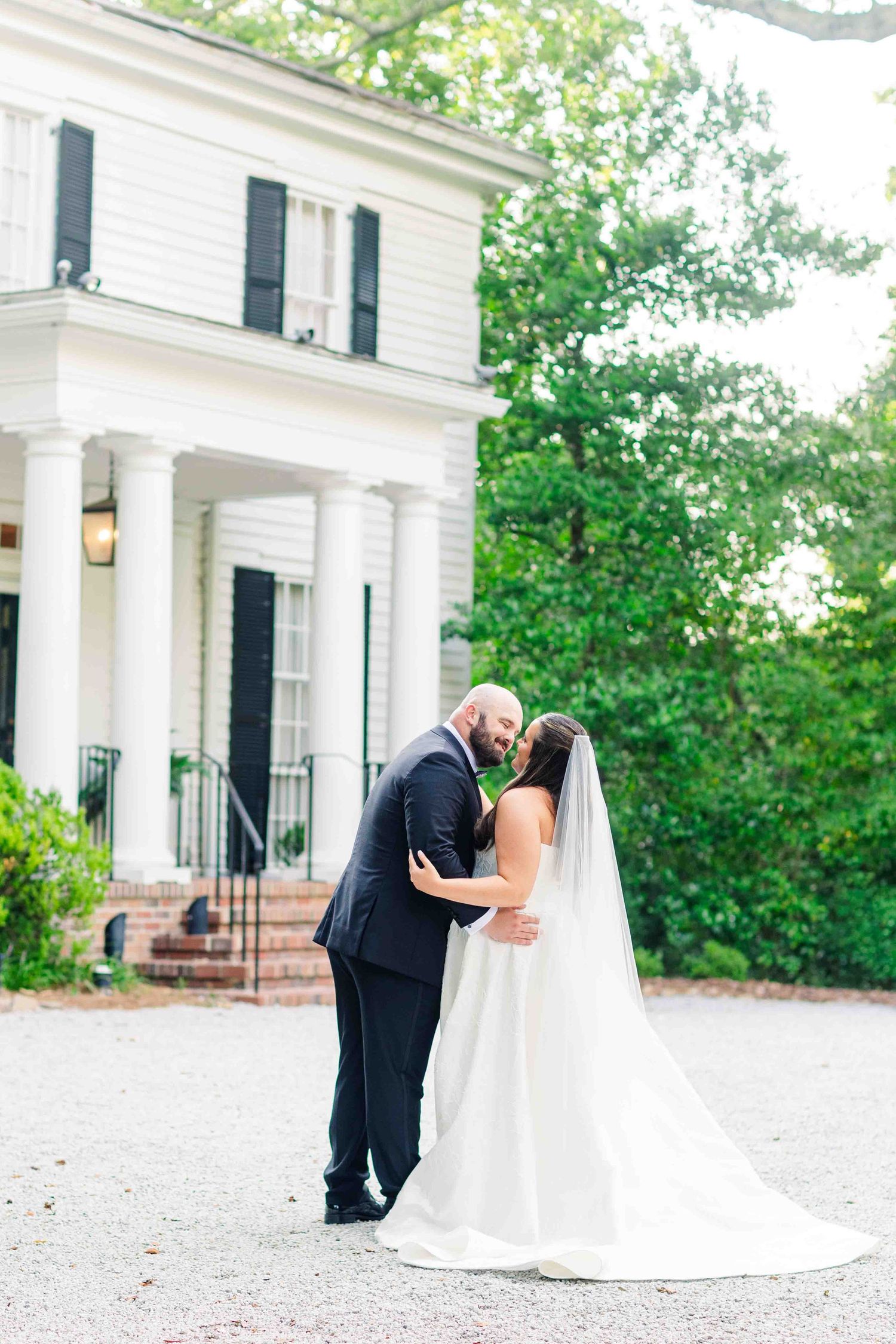 Bride and groom share a romantic kiss outside a white Southern mansion on their wedding day.
