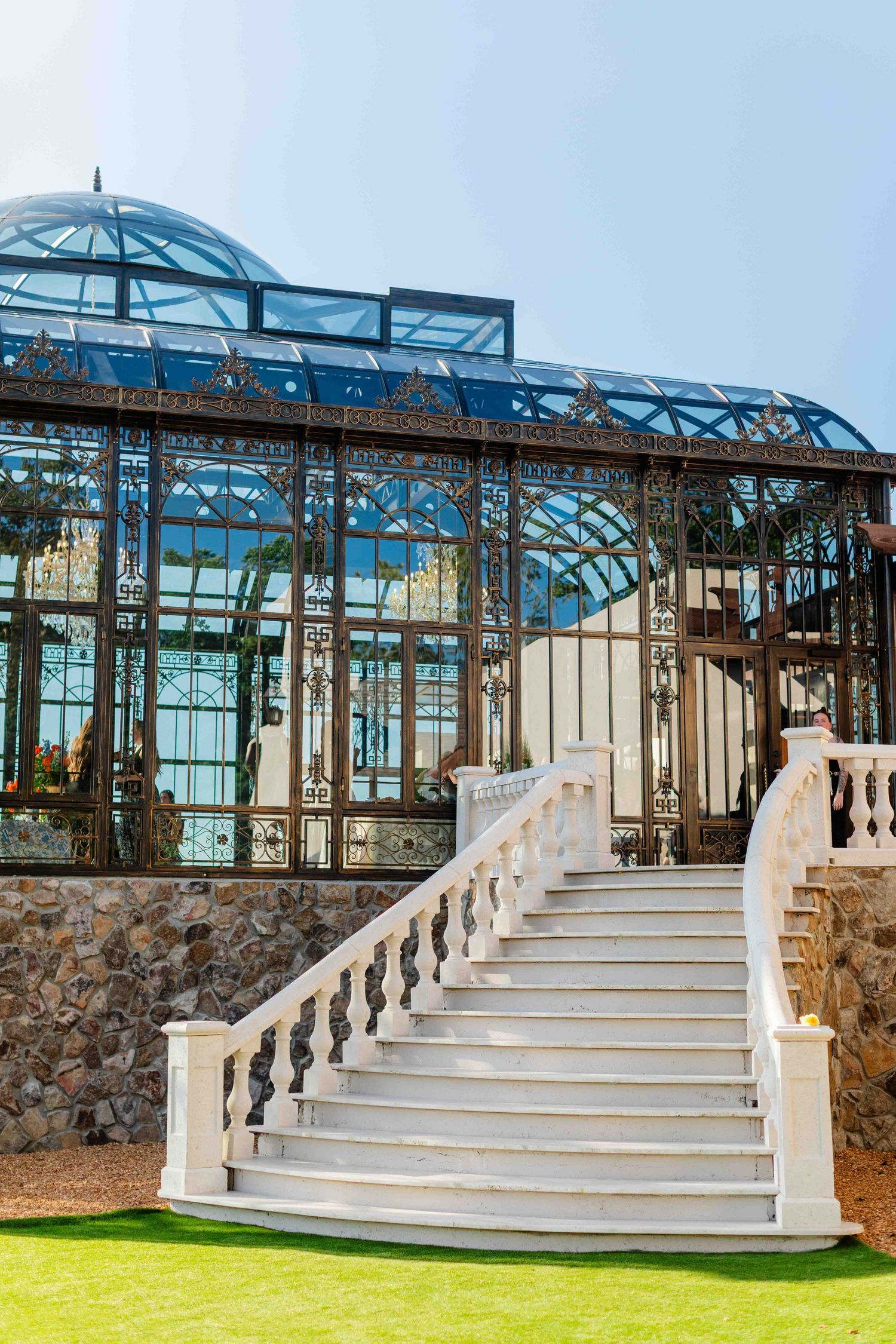 Elegant white marble staircase leading to an ornate Victorian glass greenhouse with intricate ironwork and blue dome.