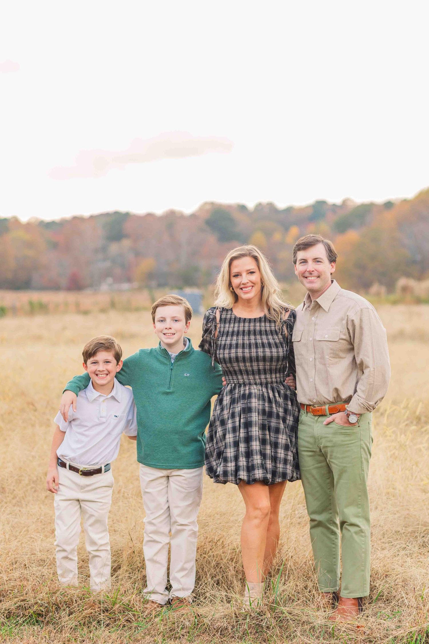 Family of four posing together in a golden autumn field at sunset.
