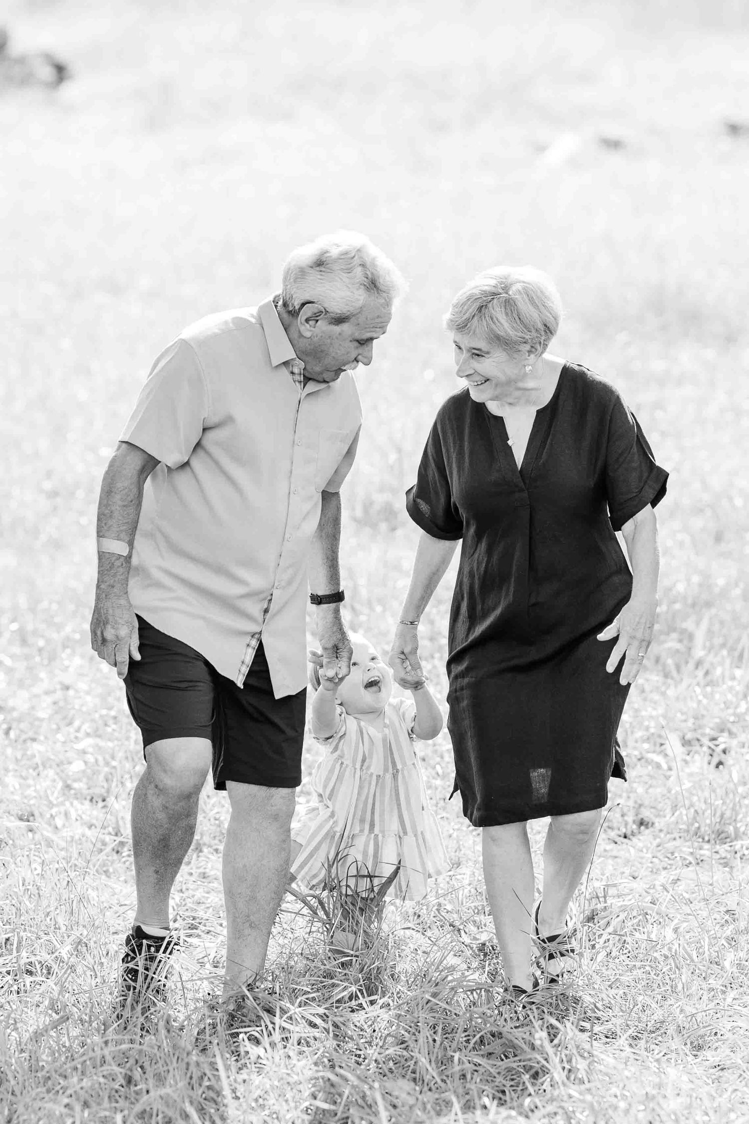 Black and white photo of happy senior couple walking together through a grassy field on a sunny day.