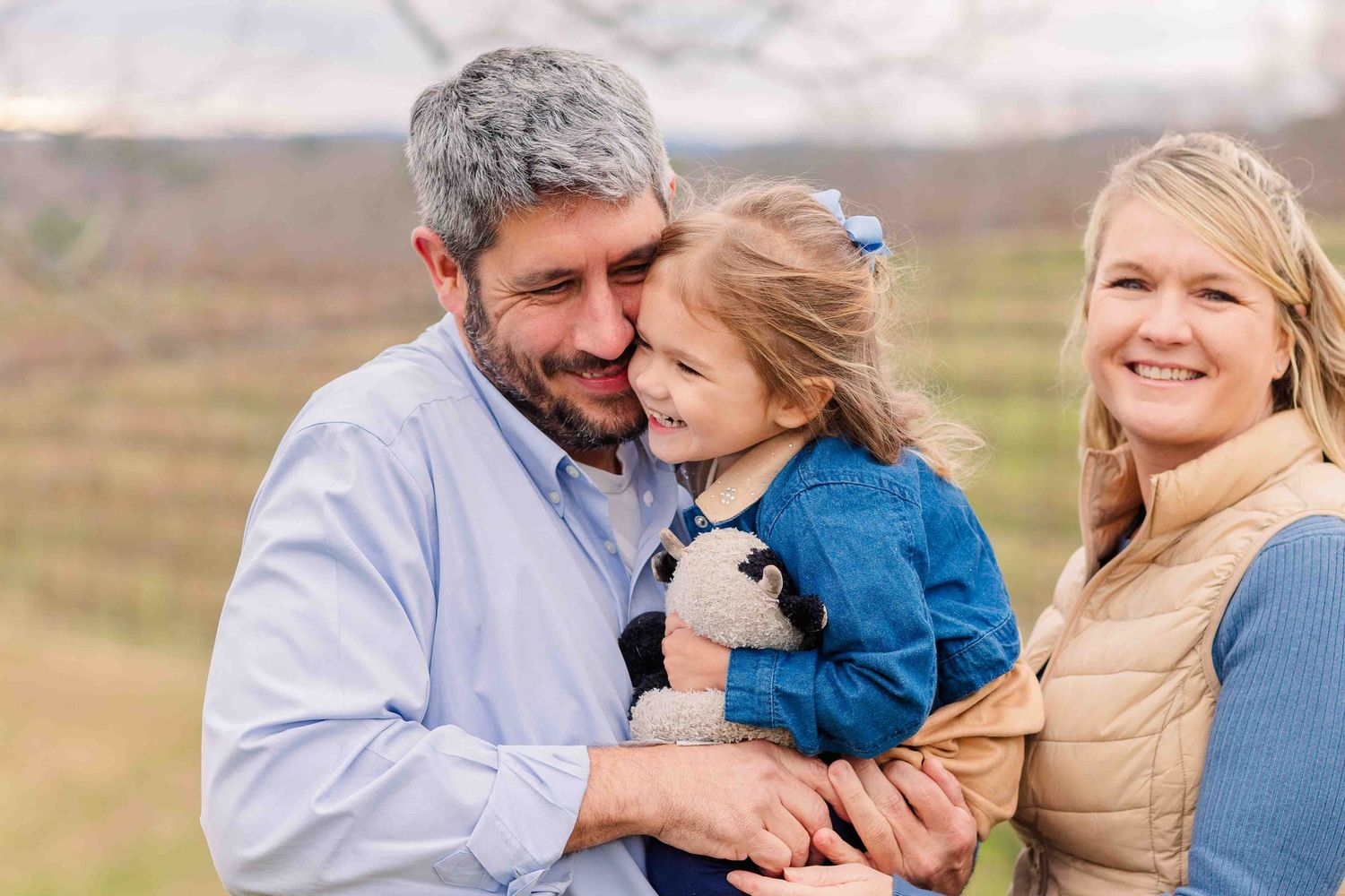 Loving family of three with father cradling young daughter while mother smiles in a vineyard.
