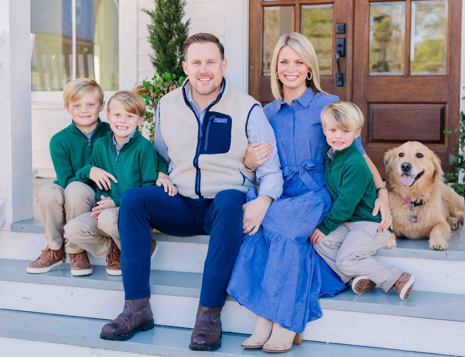 Family with three boys and a golden retriever posing on front porch steps.