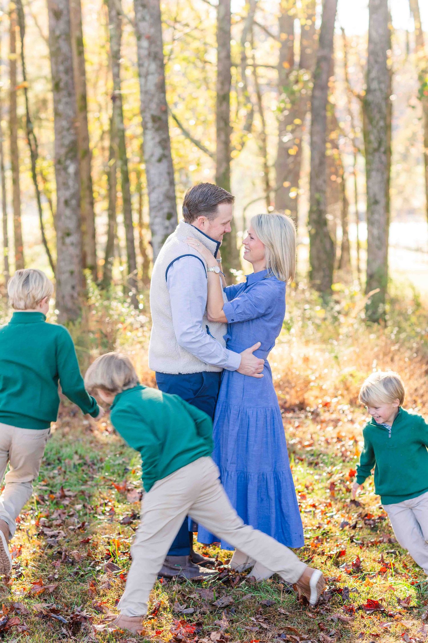 Couple embracing while three boys play around them in a colorful fall forest.