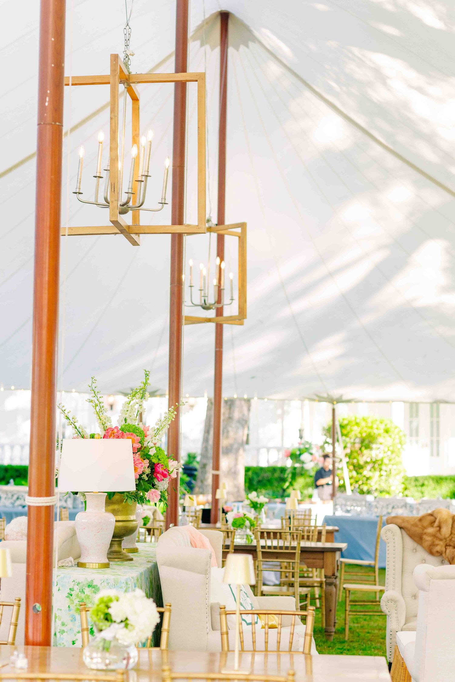 Elegant white wedding tent with gold chandeliers, floral centerpieces, and chiavari chairs.