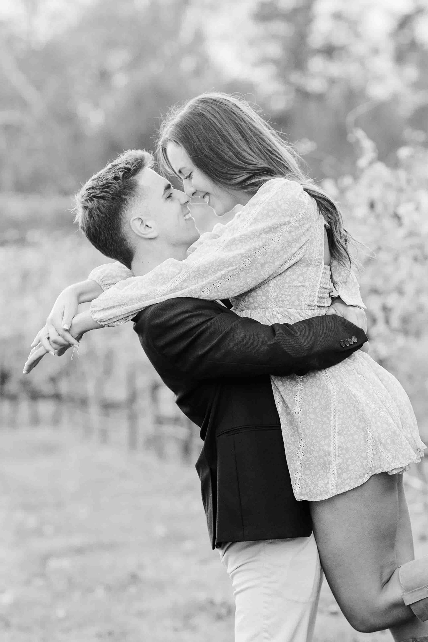 Black and white photo of man lifting and kissing woman in a romantic vineyard embrace.