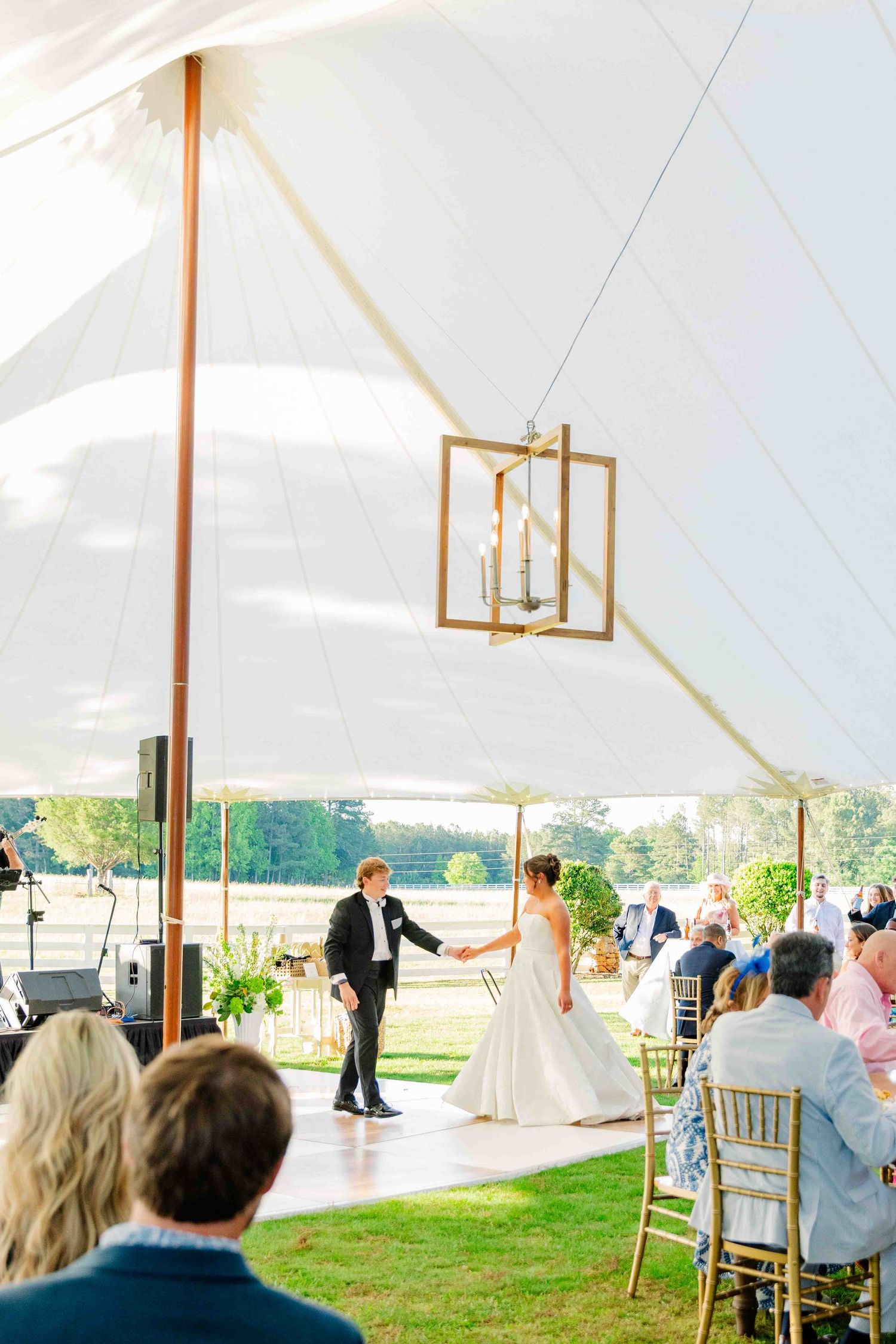 Bride and groom sharing first dance under elegant sailcloth tent with chandelier at outdoor reception.