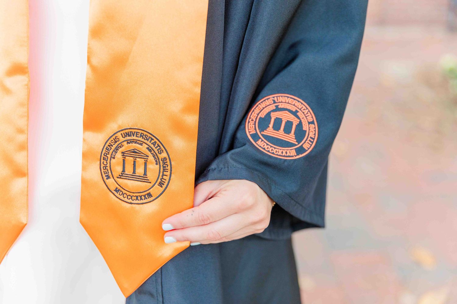 Close-up of Mercer University graduation gown sleeve with embroidered orange stole detail.