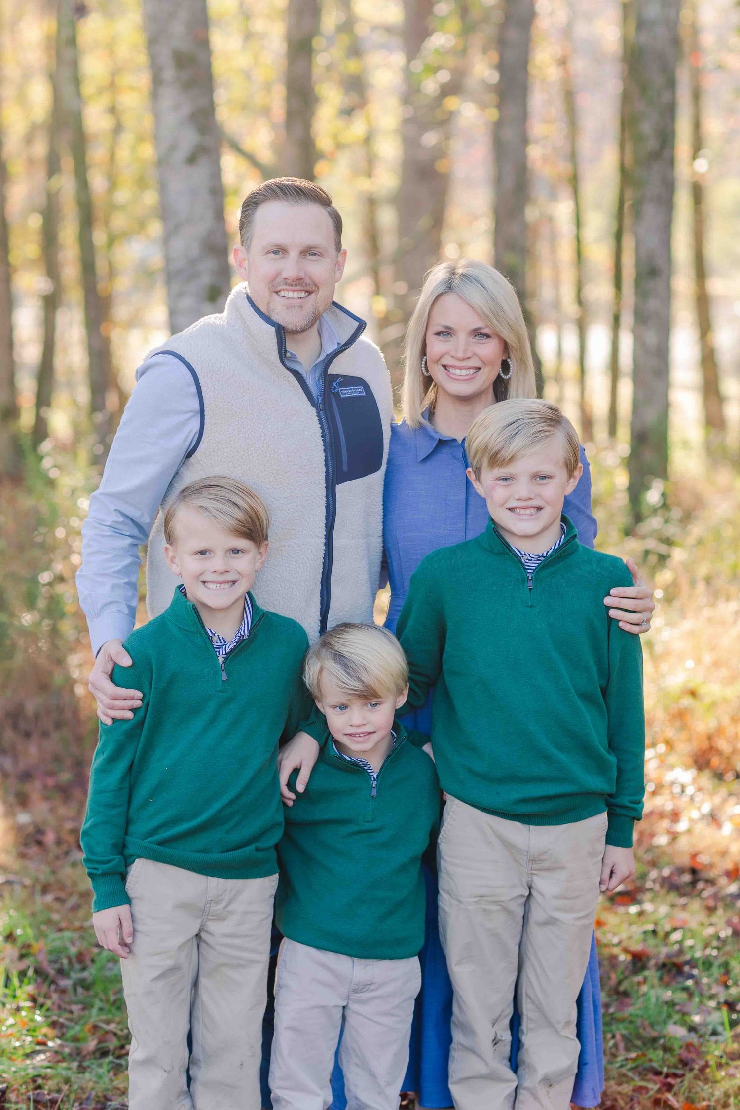 Smiling family of five with three boys wearing green pullovers in a colorful fall woodland backdrop.