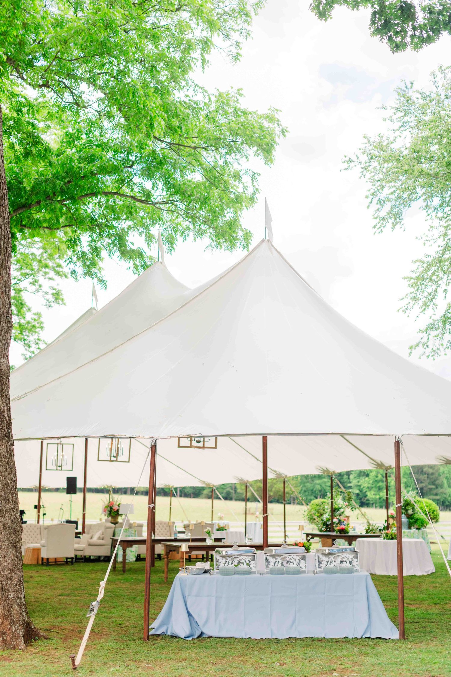 White sailcloth wedding tent set up outdoors on green lawn with reception tables underneath.