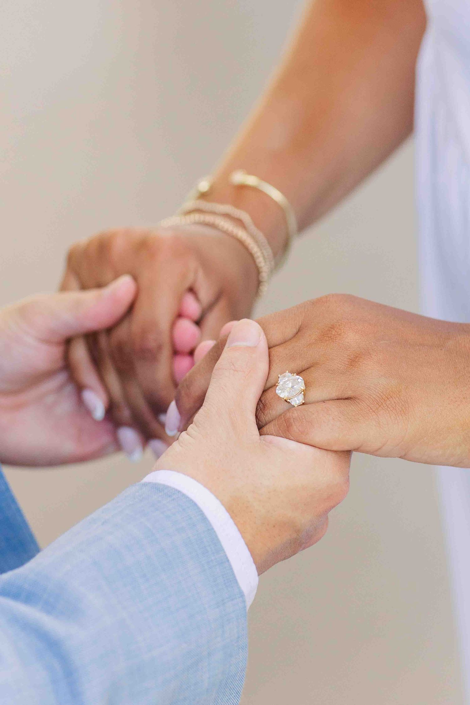 Close-up of couple holding hands, woman wearing stunning oval diamond engagement ring and gold bracelets.