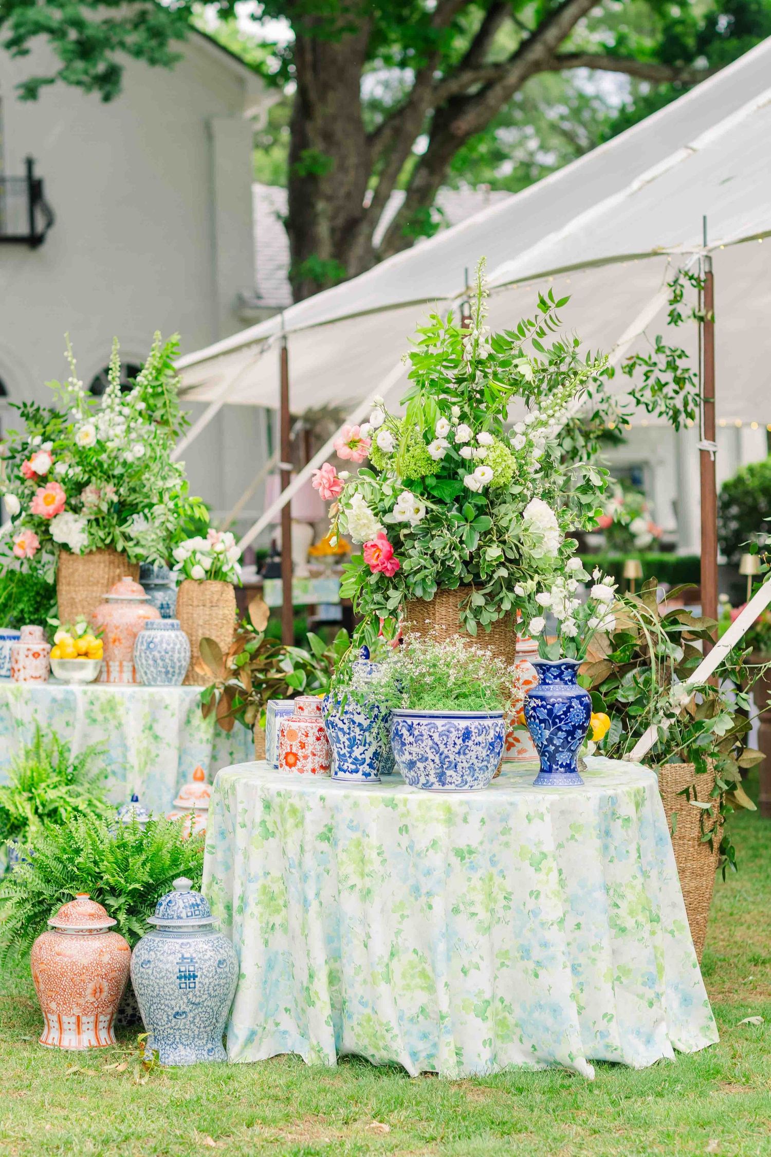 Outdoor wedding reception tables with blue and white chinoiserie vases and lush floral arrangements under tent.