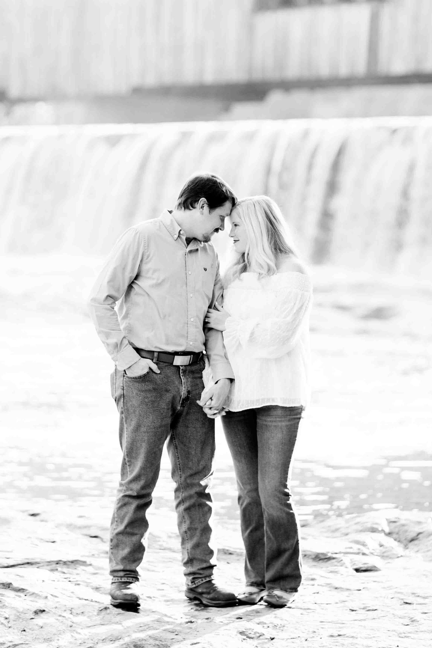 Black and white photo of a couple sharing a romantic moment near a waterfall outdoors.