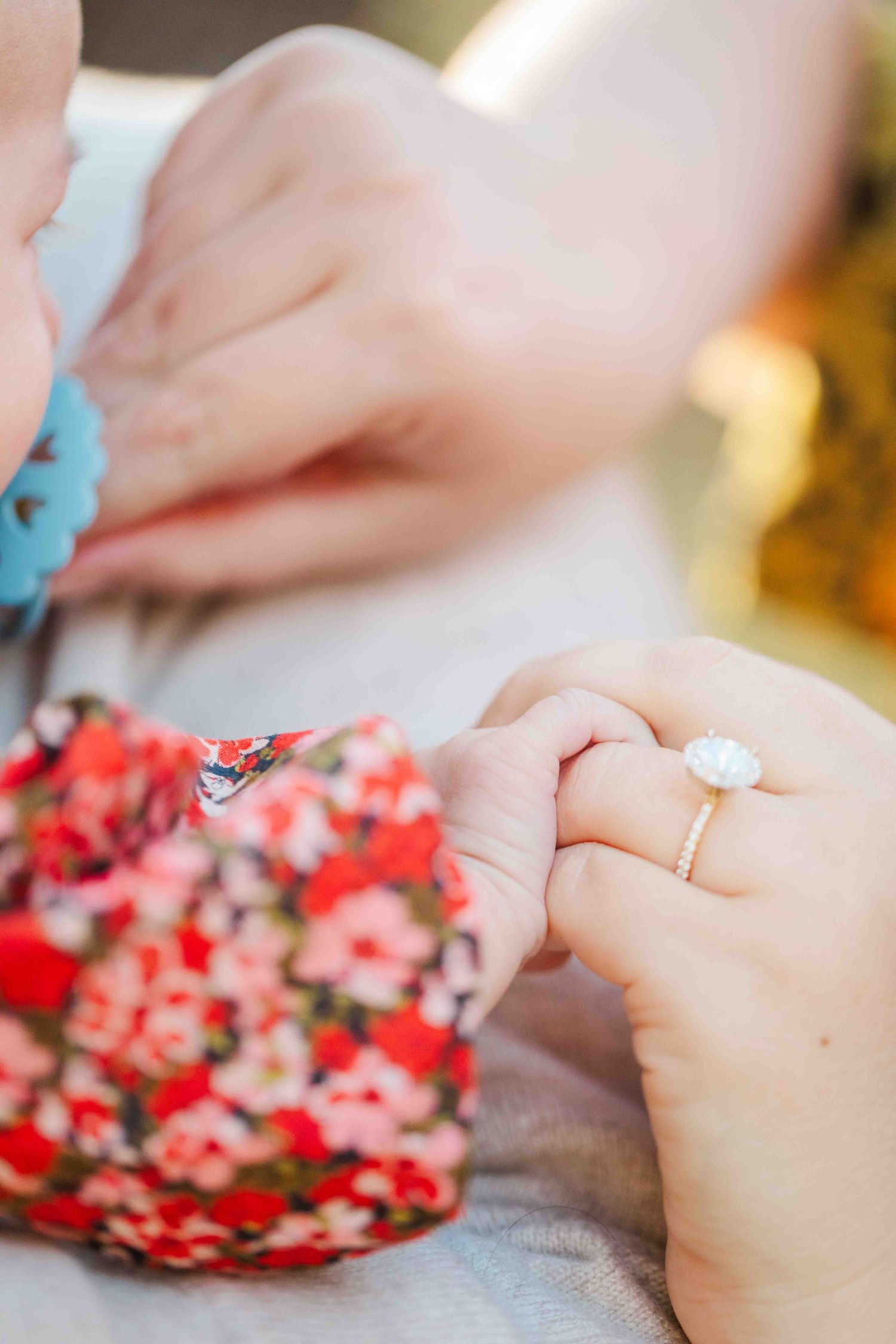 Close-up of mother holding newborn baby's hand while wearing a delicate oval diamond engagement ring.