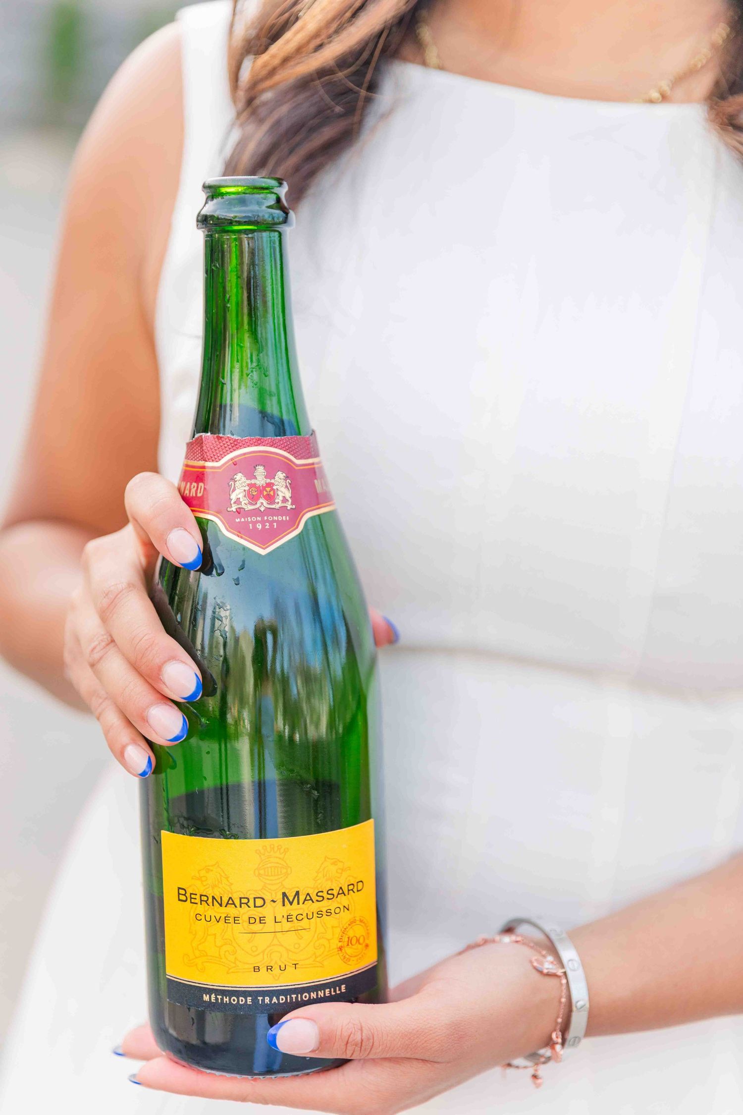 Woman in white dress holding a Bernard-Massard Cuvée de l'Ecusson Brut sparkling wine bottle.