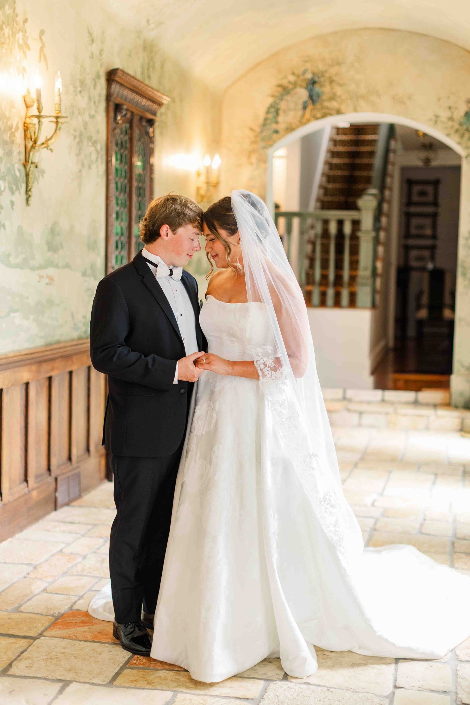 Bride and groom share an intimate moment in a beautifully decorated indoor venue with mural walls and warm candlelight.