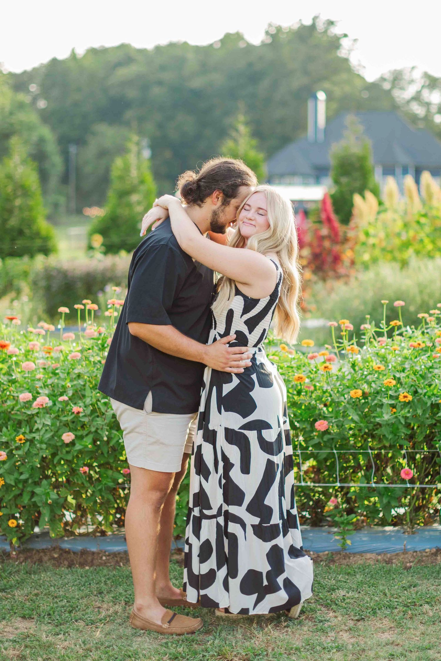 Couple hugging warmly in a colorful flower garden at golden hour, woman in black and white dress.