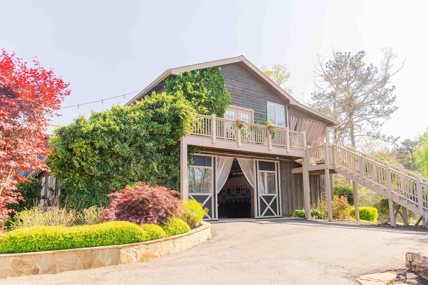 Charming two-story gray wooden wedding venue with lush green ivy, red maple trees, and a welcoming barn-style entrance.