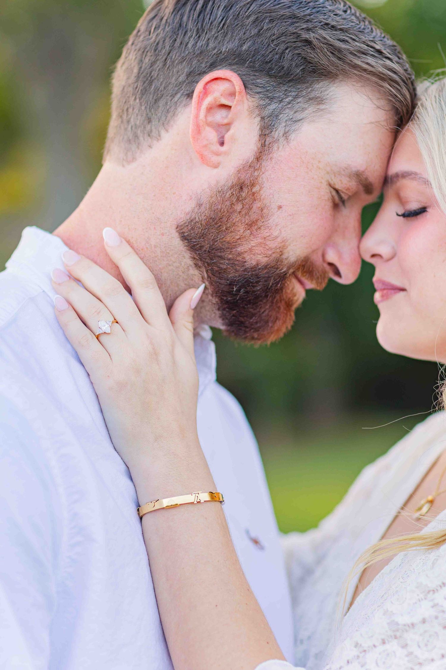 Close-up of engaged couple touching foreheads, woman showing diamond ring and gold bracelet.