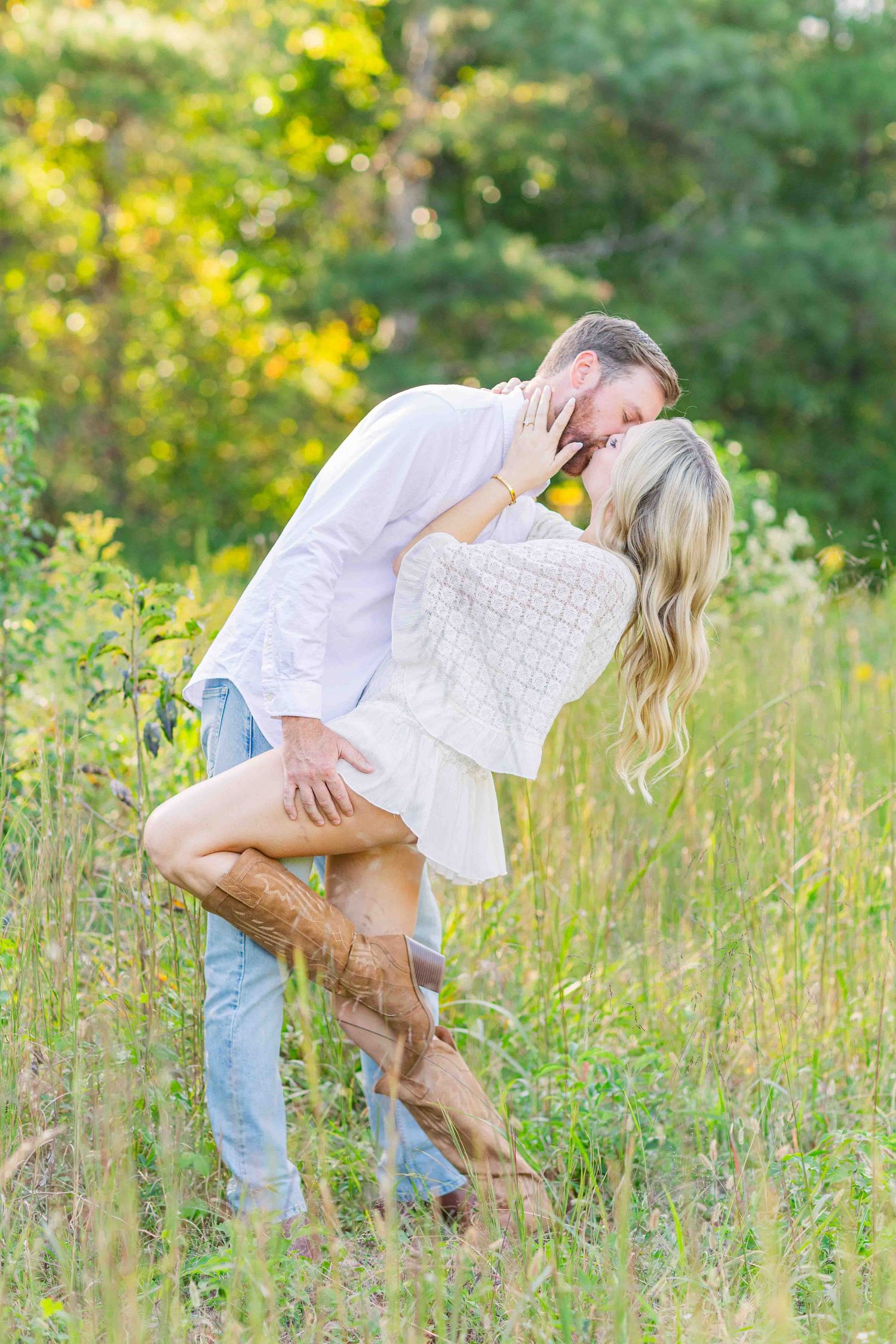 Man dipping woman for a kiss in a wildflower meadow, woman wearing cowboy boots and white dress.