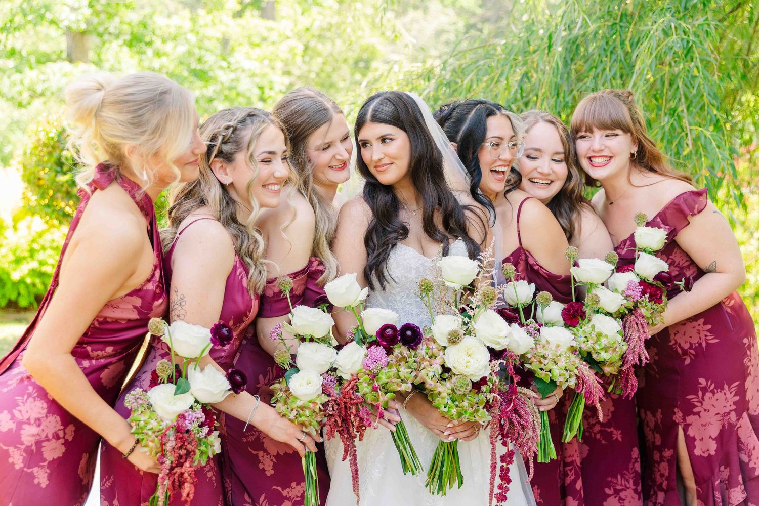 Bride with bridesmaids in burgundy dresses holding white and green wedding bouquets.