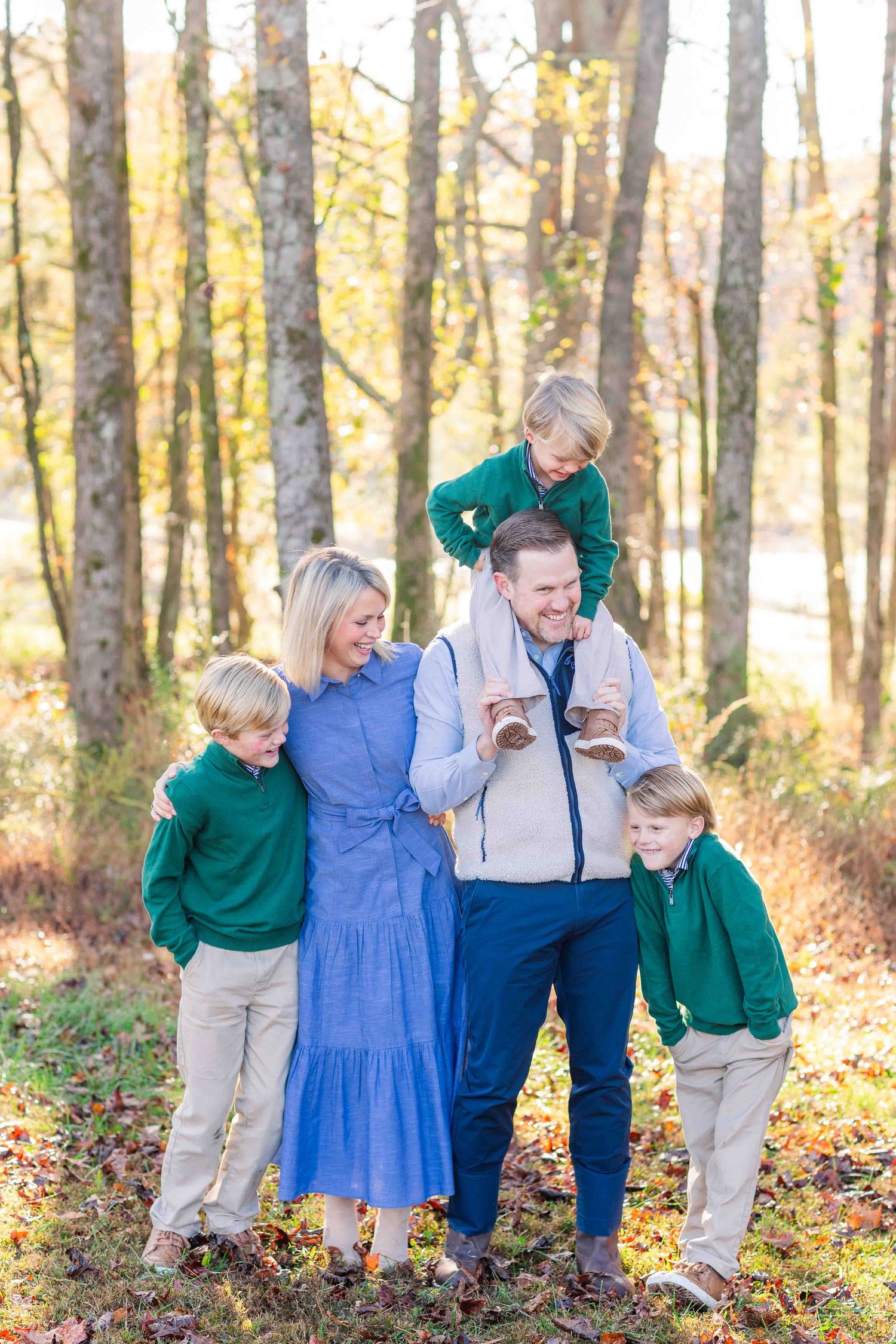 Joyful family laughing together in fall woodland setting with children in matching outfits.