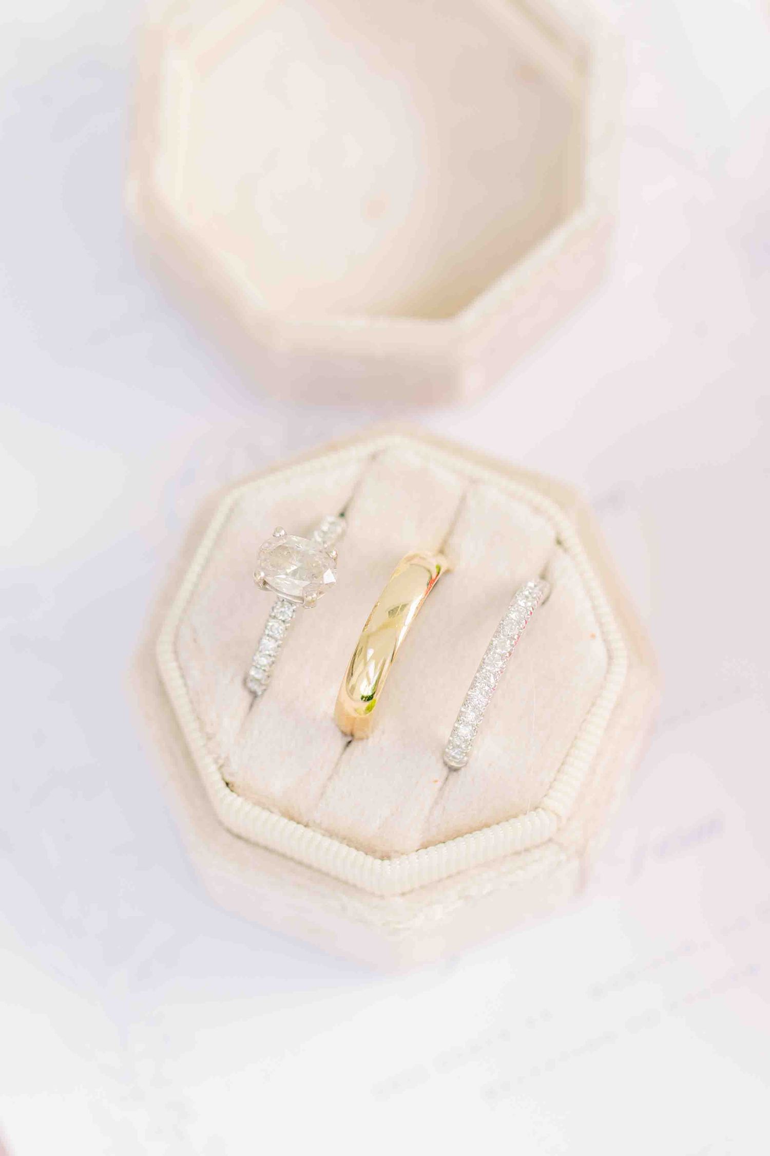 Three elegant rings displayed in a blush velvet octagonal ring box, featuring diamond bands and a gold band.