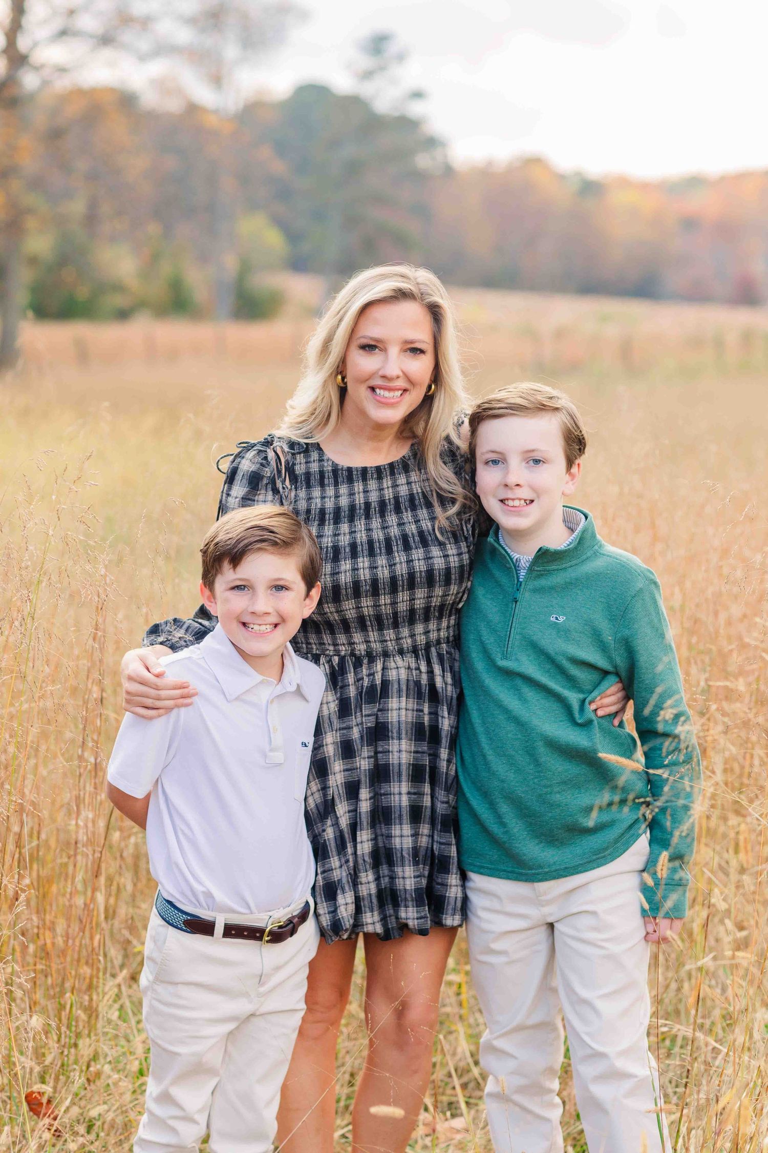 Blonde mother posing with two young sons in an autumn field with golden grass.