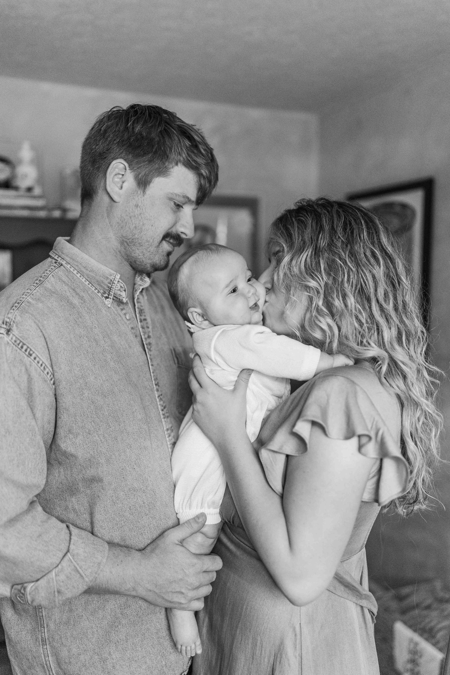 Black and white photo of young parents lovingly gazing at their newborn baby together indoors.