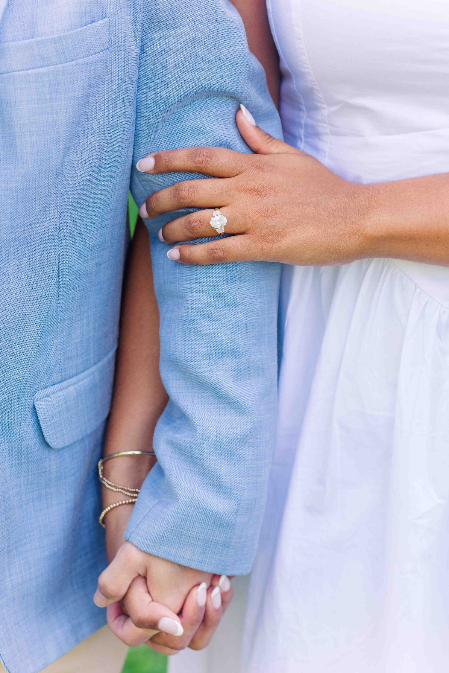 Close-up of woman's hand wearing large oval diamond engagement ring while holding man's arm in blue blazer.