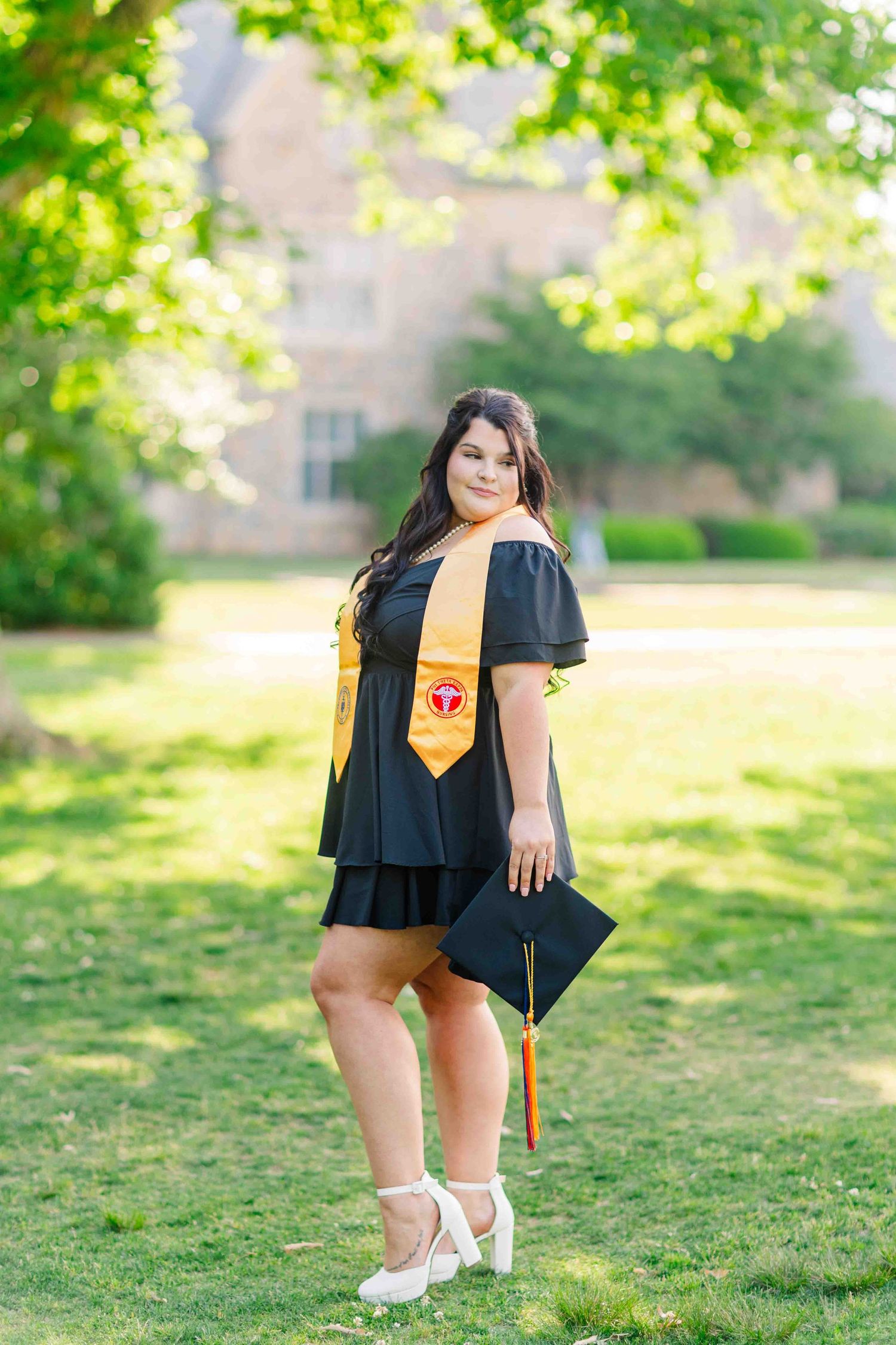 Graduate in black cap and gown with gold stole posing outdoors on university campus.