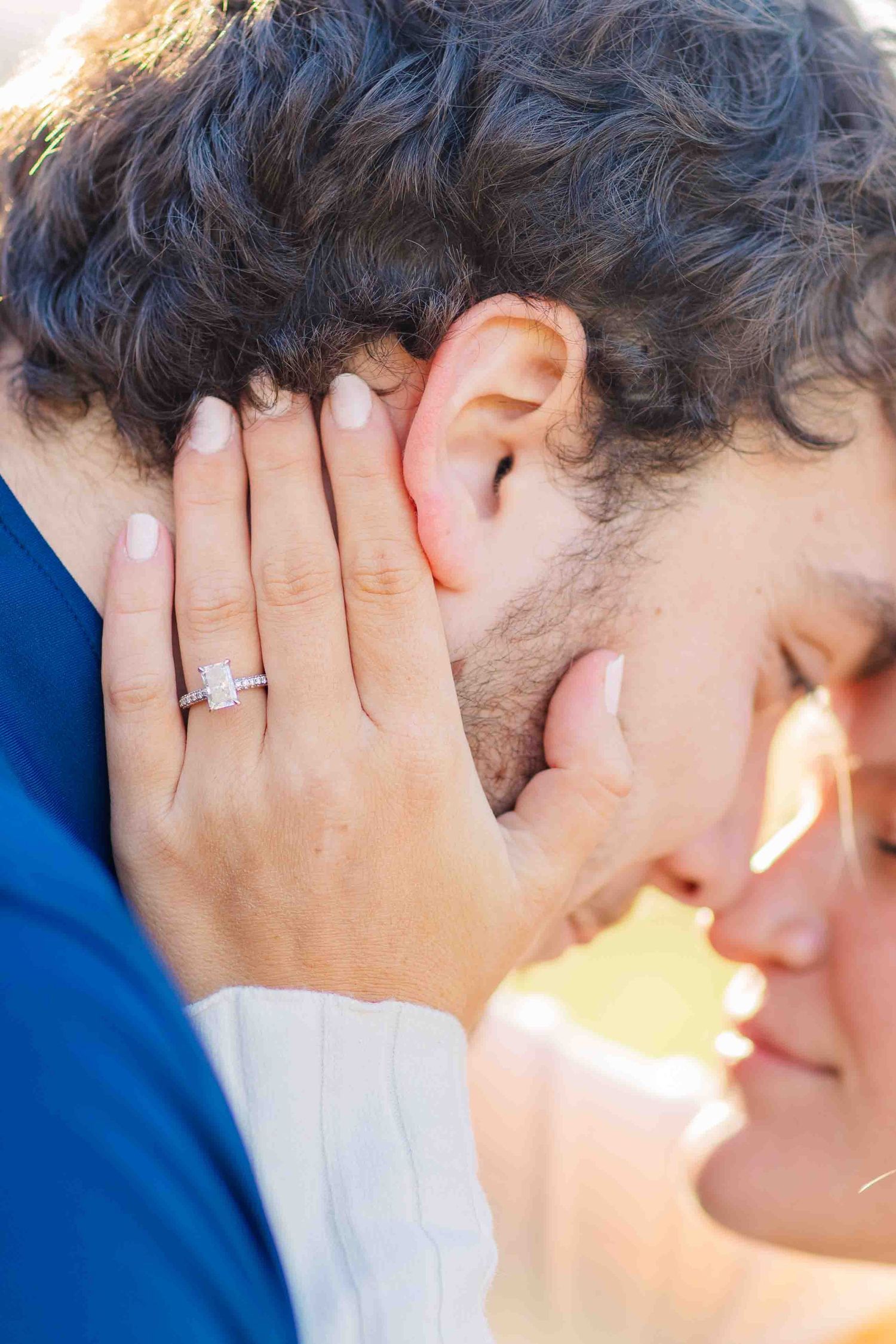 Close-up of couple nearly kissing with focus on woman's elegant emerald-cut diamond engagement ring.