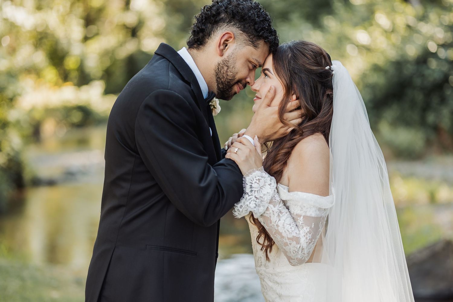 Bride and groom sharing intimate forehead touch moment near water on wedding day.