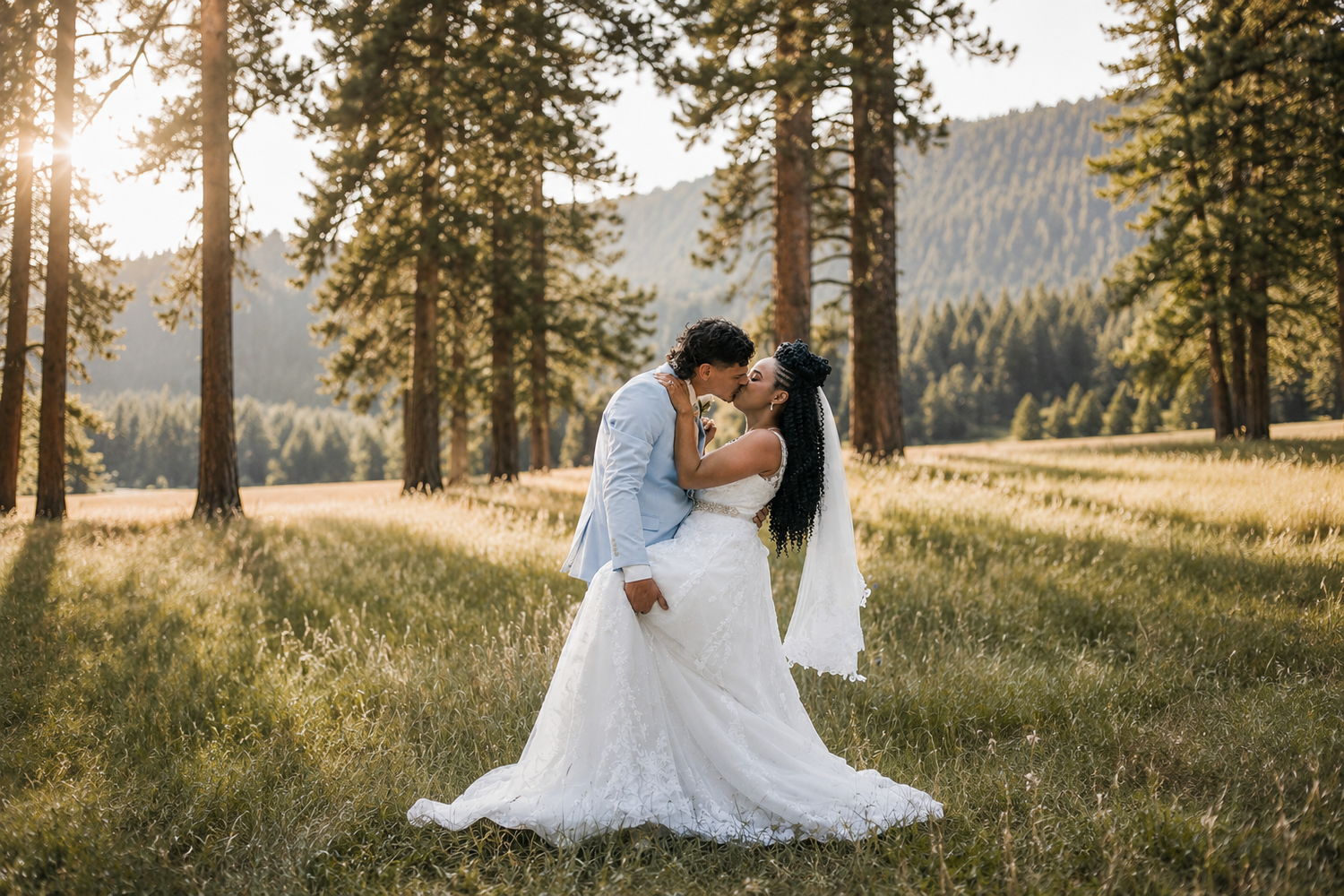 Bride and groom sharing romantic kiss in sunlit meadow surrounded by tall pine trees.