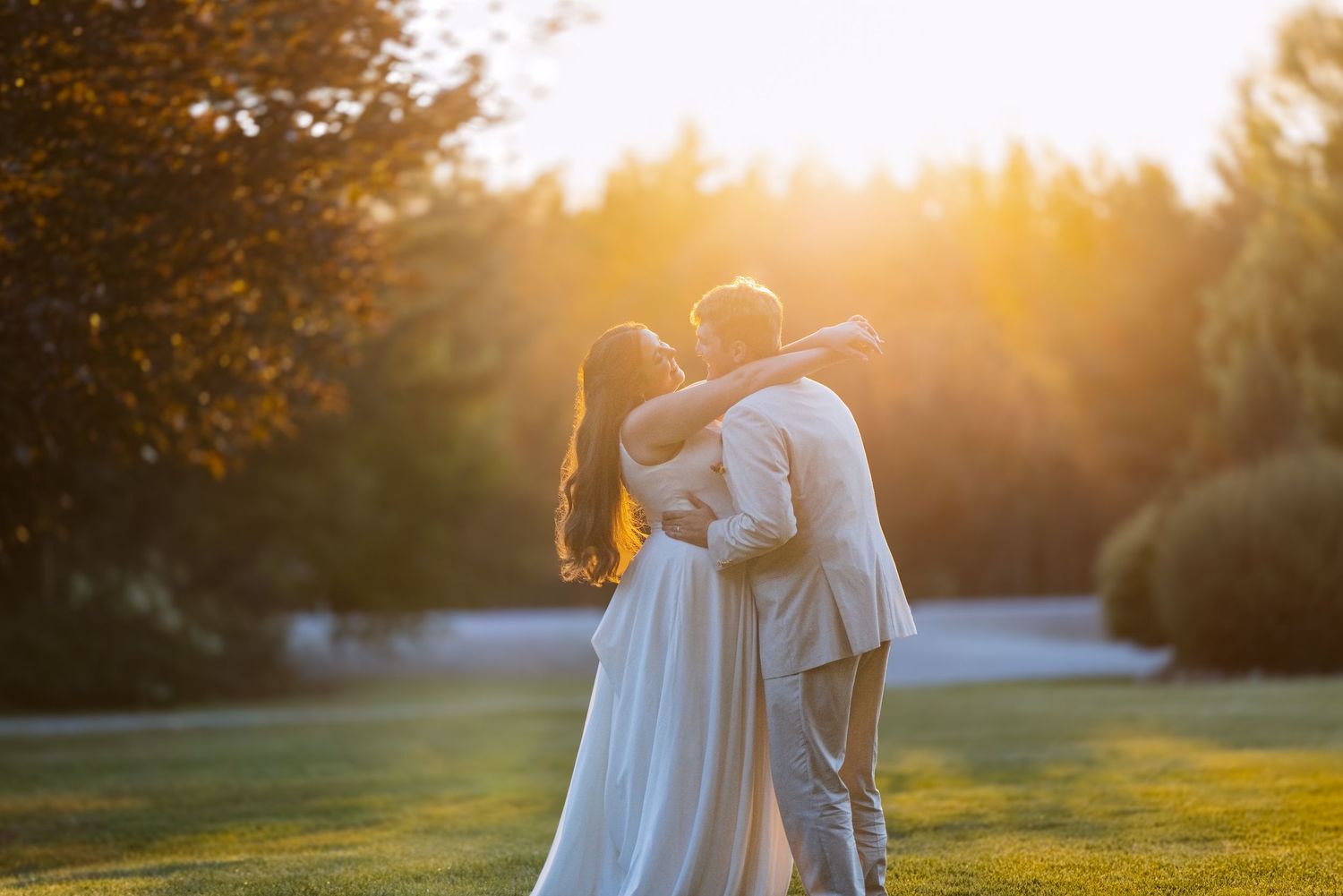 Bride and groom embracing in golden sunset light in lush garden setting.