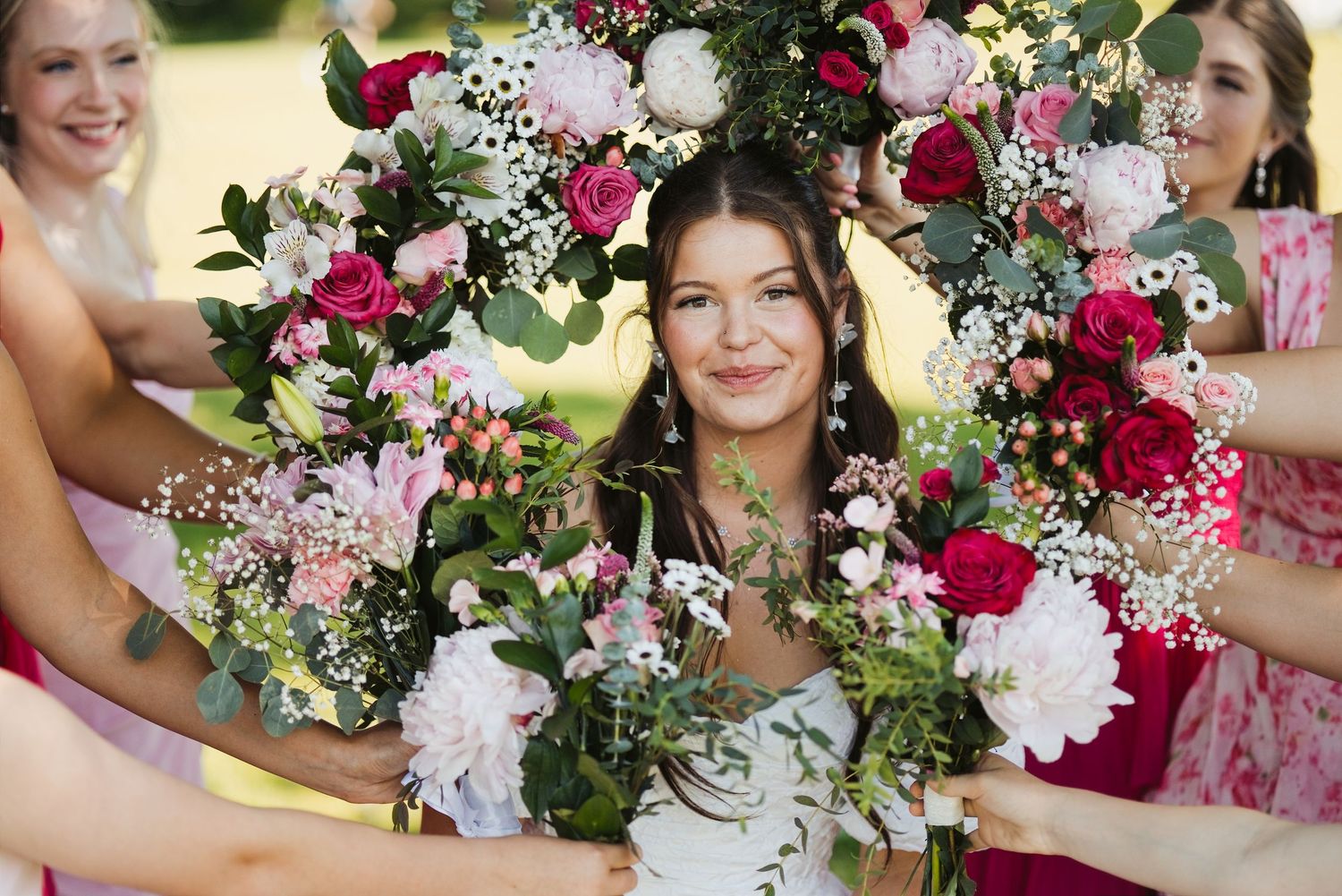 Bride surrounded by bridesmaids holding colorful pink and red floral bouquets together.