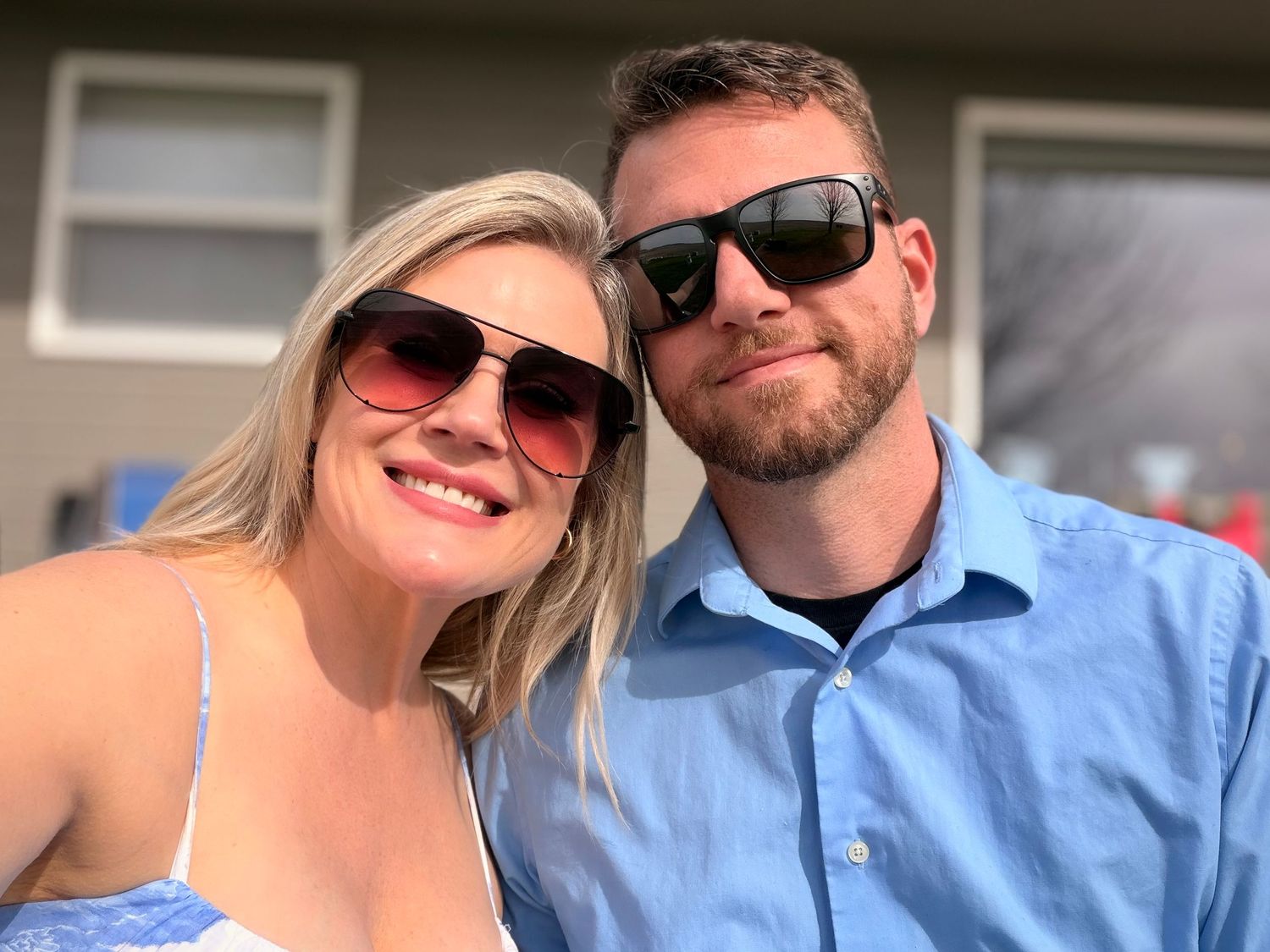 Smiling couple wearing sunglasses posing together outdoors on a sunny day.