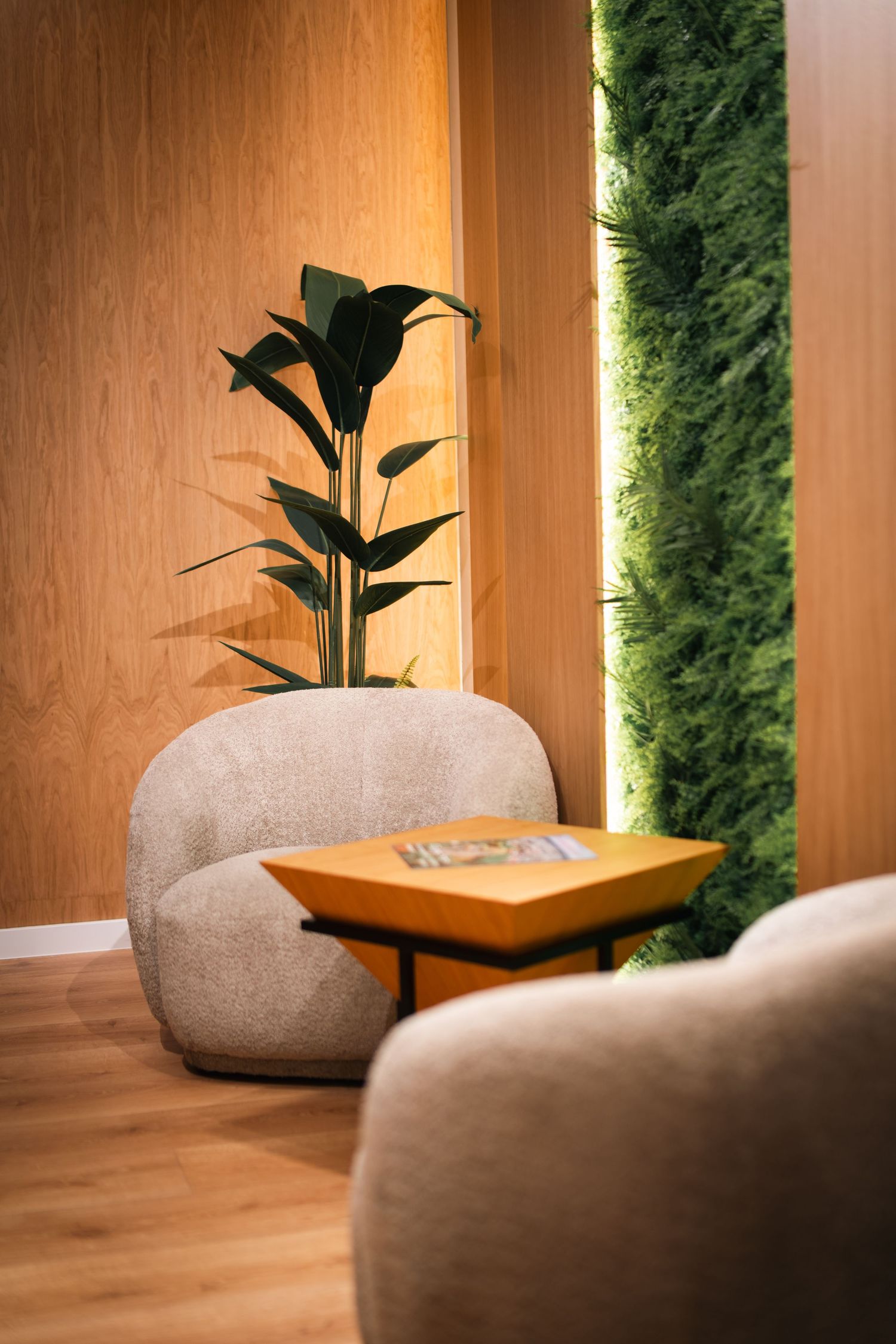 Cozy hotel lounge corner with round beige armchair, tropical plant, and green moss wall accent panel.
