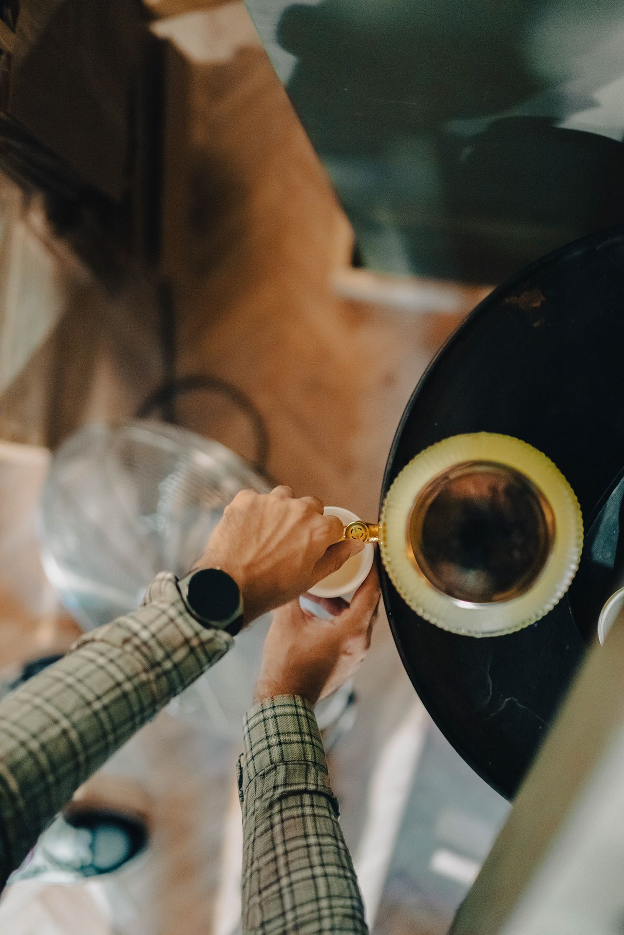 Overhead view of hands holding espresso cup on black tray in a coffee shop setting.