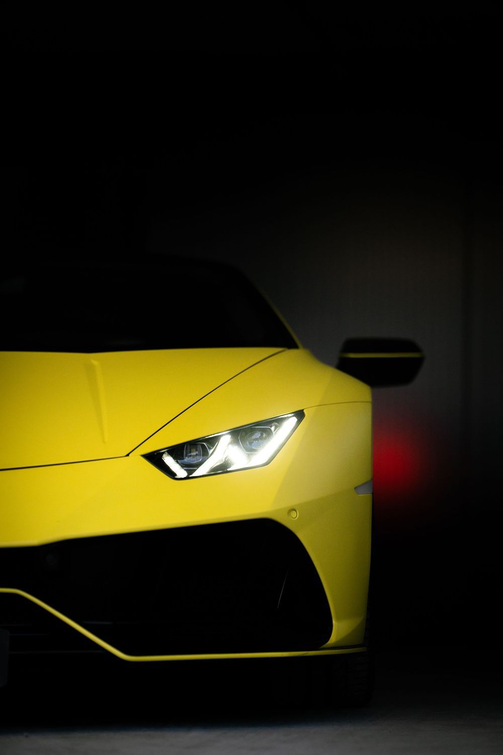 Yellow Lamborghini Huracan sports car headlight detail in dramatic dark studio lighting.