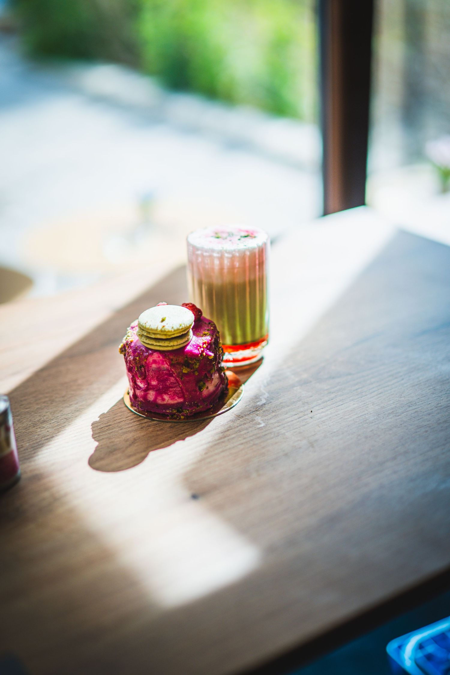 Dragon fruit dessert and layered matcha drink bathed in sunlight on wooden cafe table.
