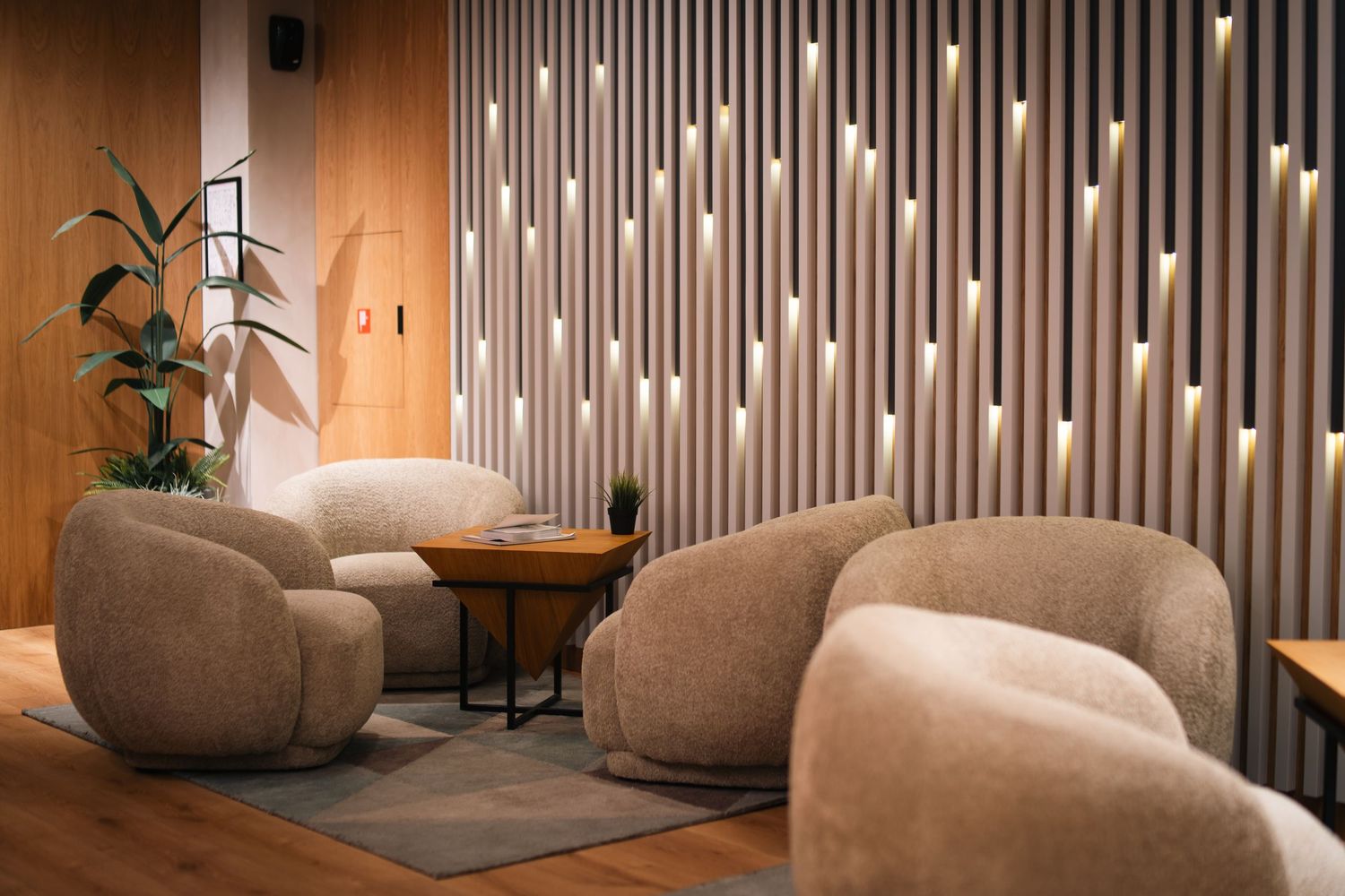 Stylish hotel lounge with beige rounded sofas, decorative wall lighting strips, and warm wood accents.
