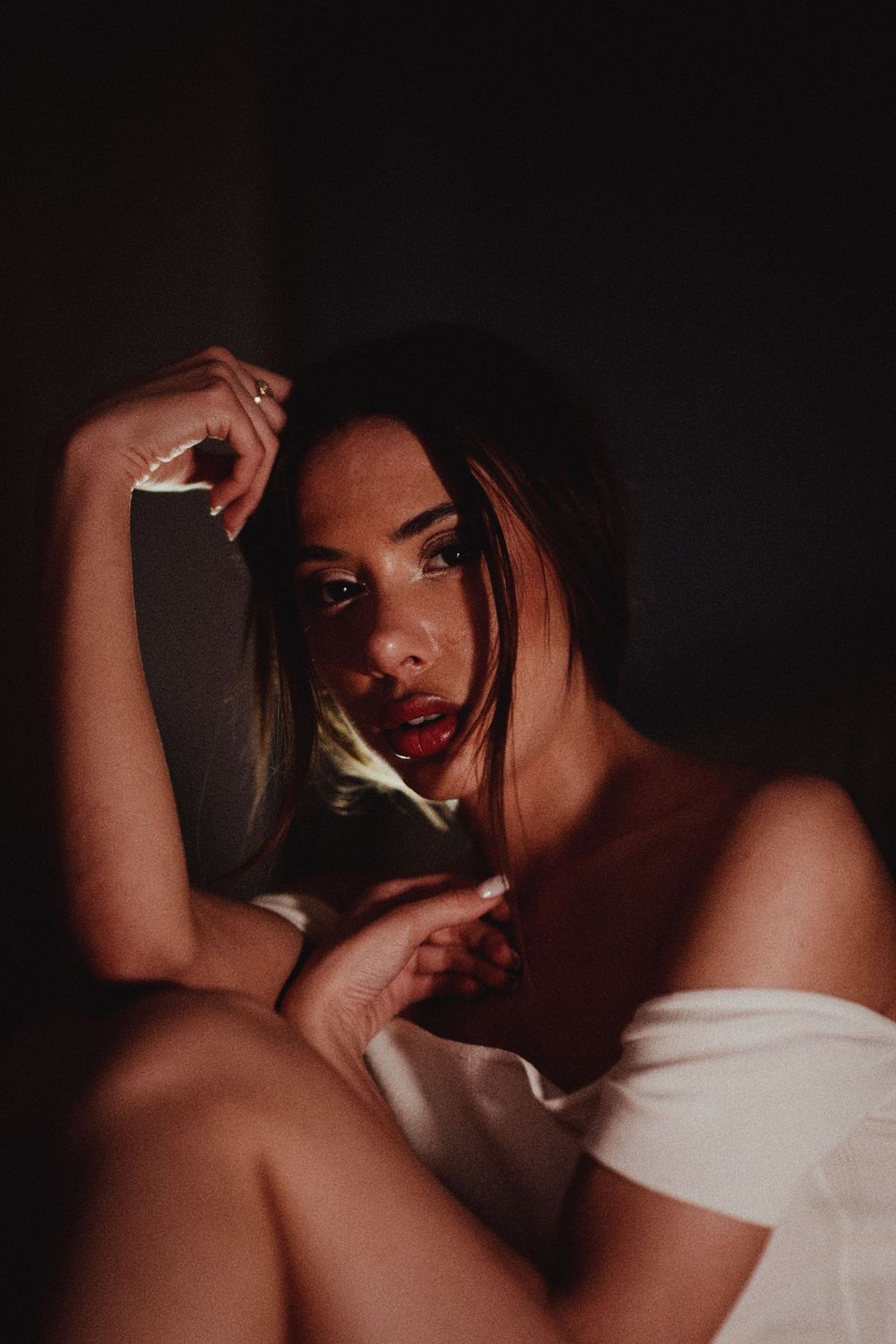 A young woman in a white wrap poses dramatically in moody low-key lighting with a dark background.