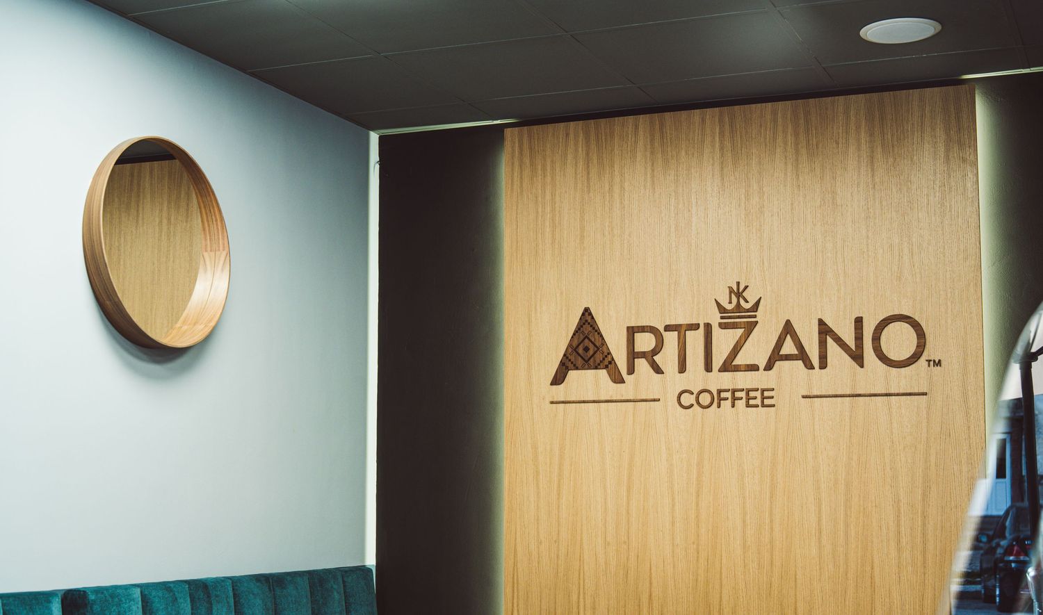 Artizano Coffee shop interior featuring wooden wall with engraved logo and circular mirror.